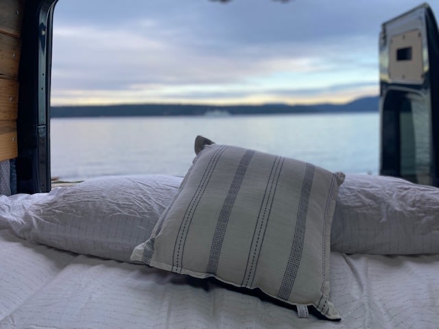 Inside this RV rental, a comfy bed provides a serene view of calm waters & distant land through the open doors.. Mercedes Sprinter Van 2017