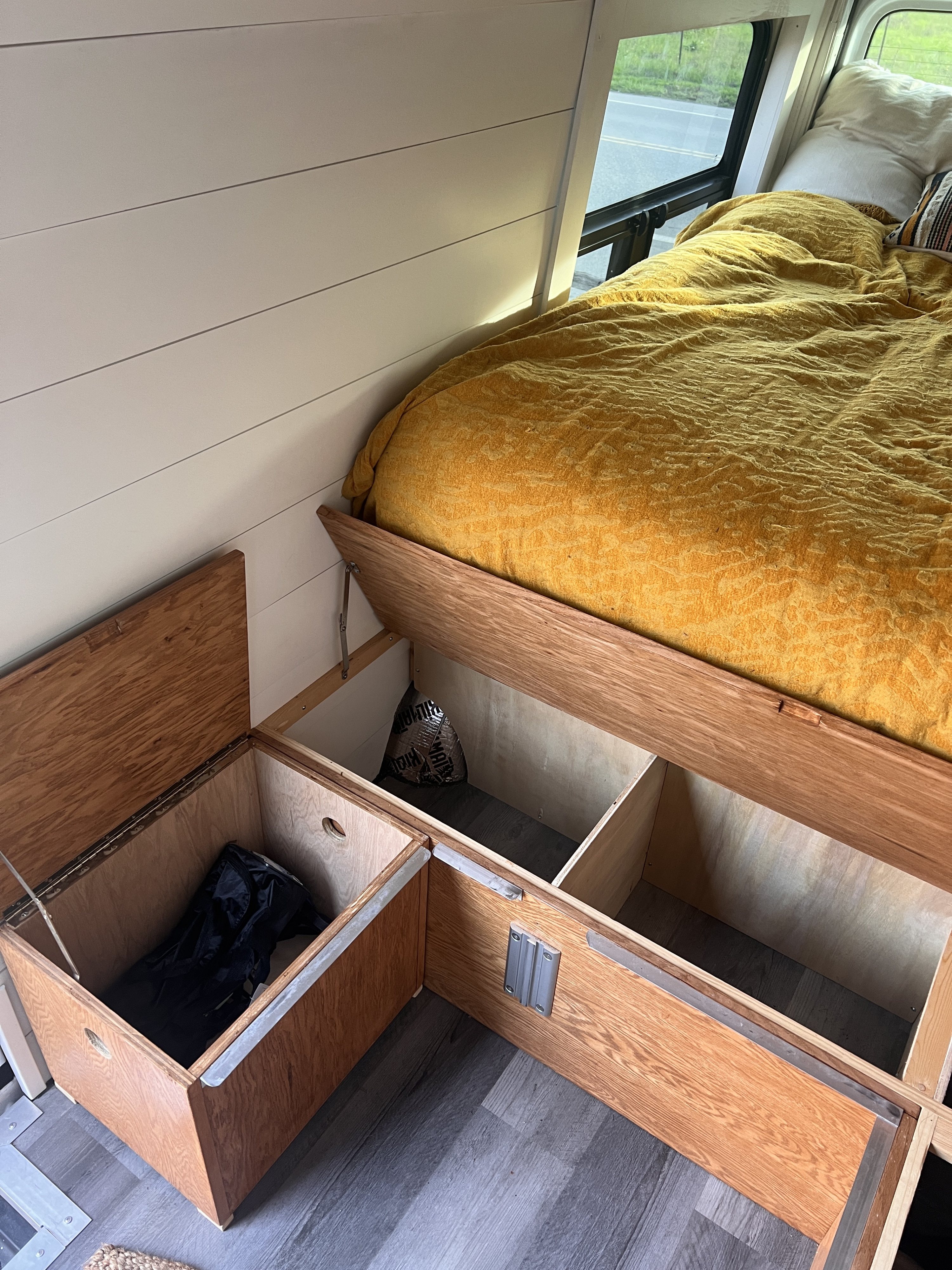 RV rental: Cozy bed with yellow comforter & built-in wood storage in a camper van, with a roadside view.. Mercedes-Benz Sprinter 2013
