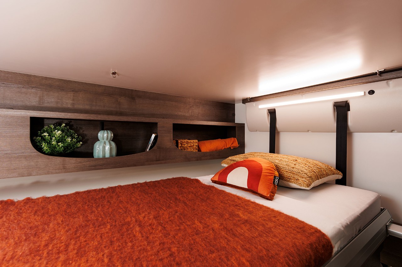 Cozy RV rental bedroom with warm orange bedding, integrated shelving, and LED lighting for comfortable travel.. Benimar Sport 340 UP 2024