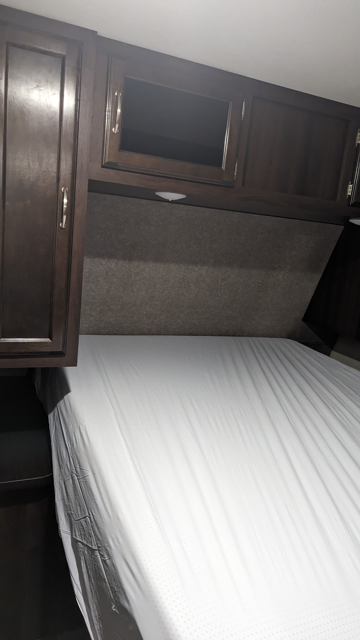 Interior of a clean RV rental bedroom, featuring dark wood cabinets, a grey headboard, and a white mattress.. Jayco Jay Flight 2018