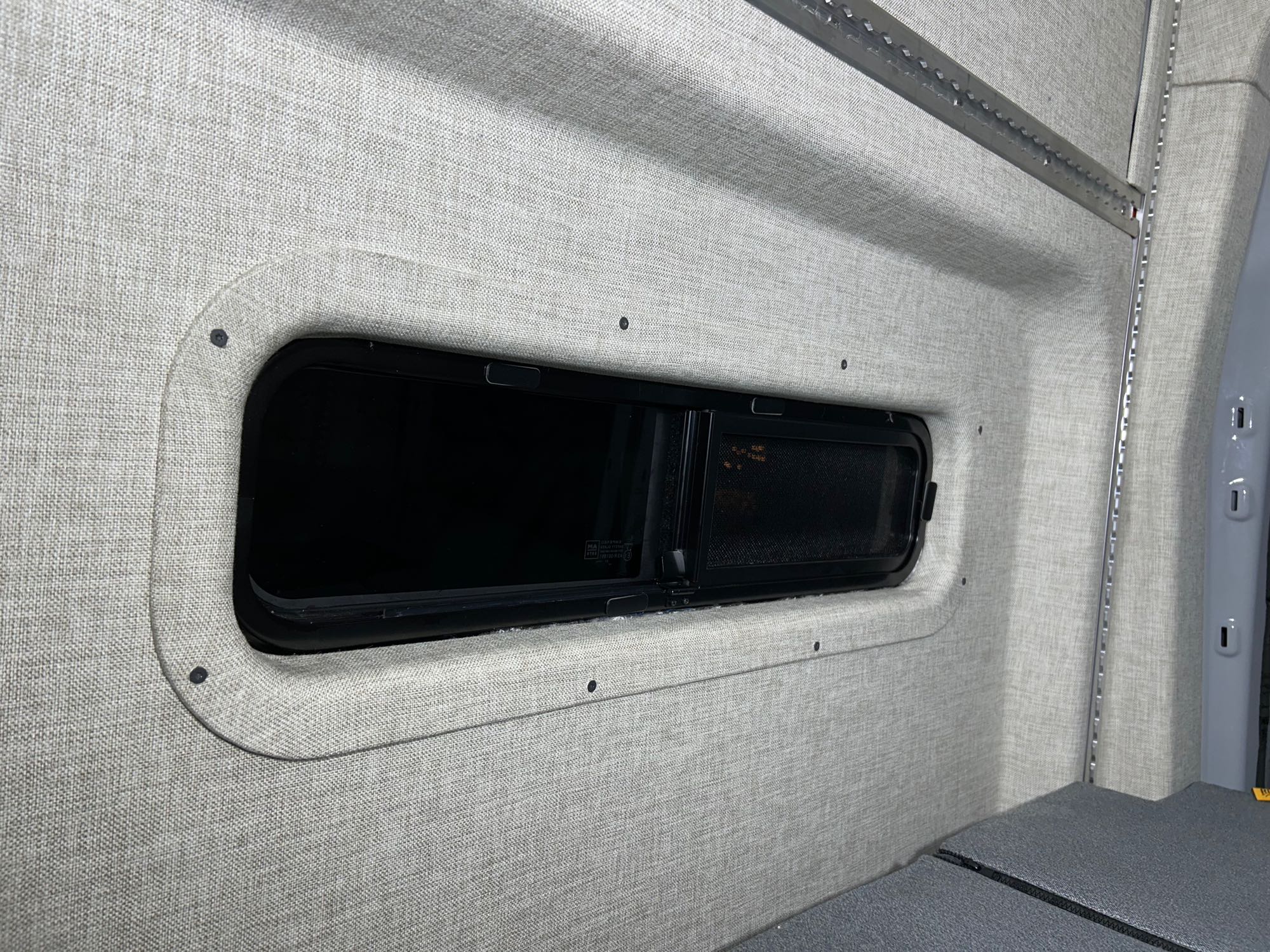 RV rental camper van interior featuring soft fabric walls, a modern window, and integrated L-track storage.. Ford Transit 2023