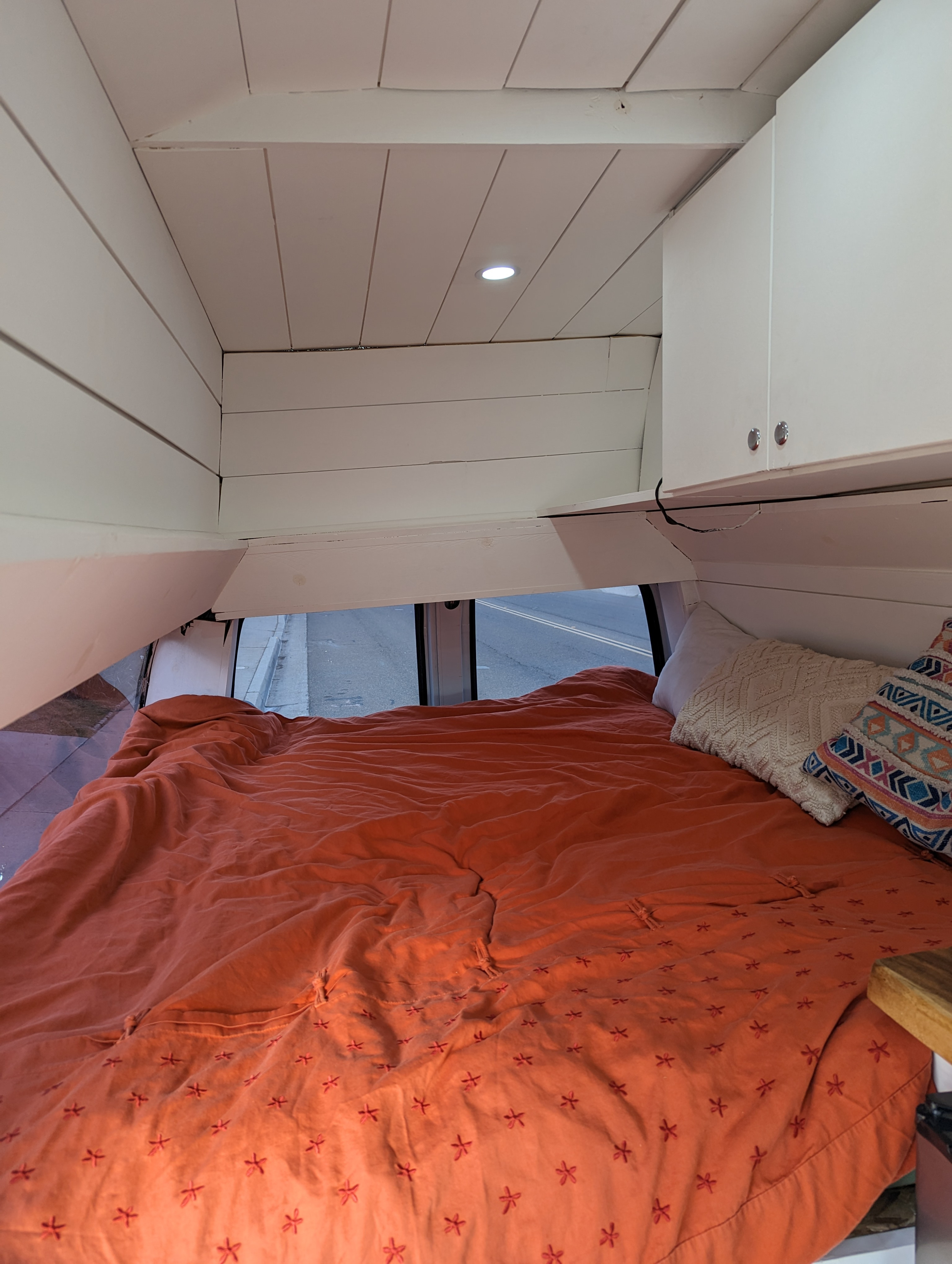 Cozy RV rental interior with bed, white paneling, and cabinets, offering a comfy sleeping area in a camper van.. Chevrolet Other 2002