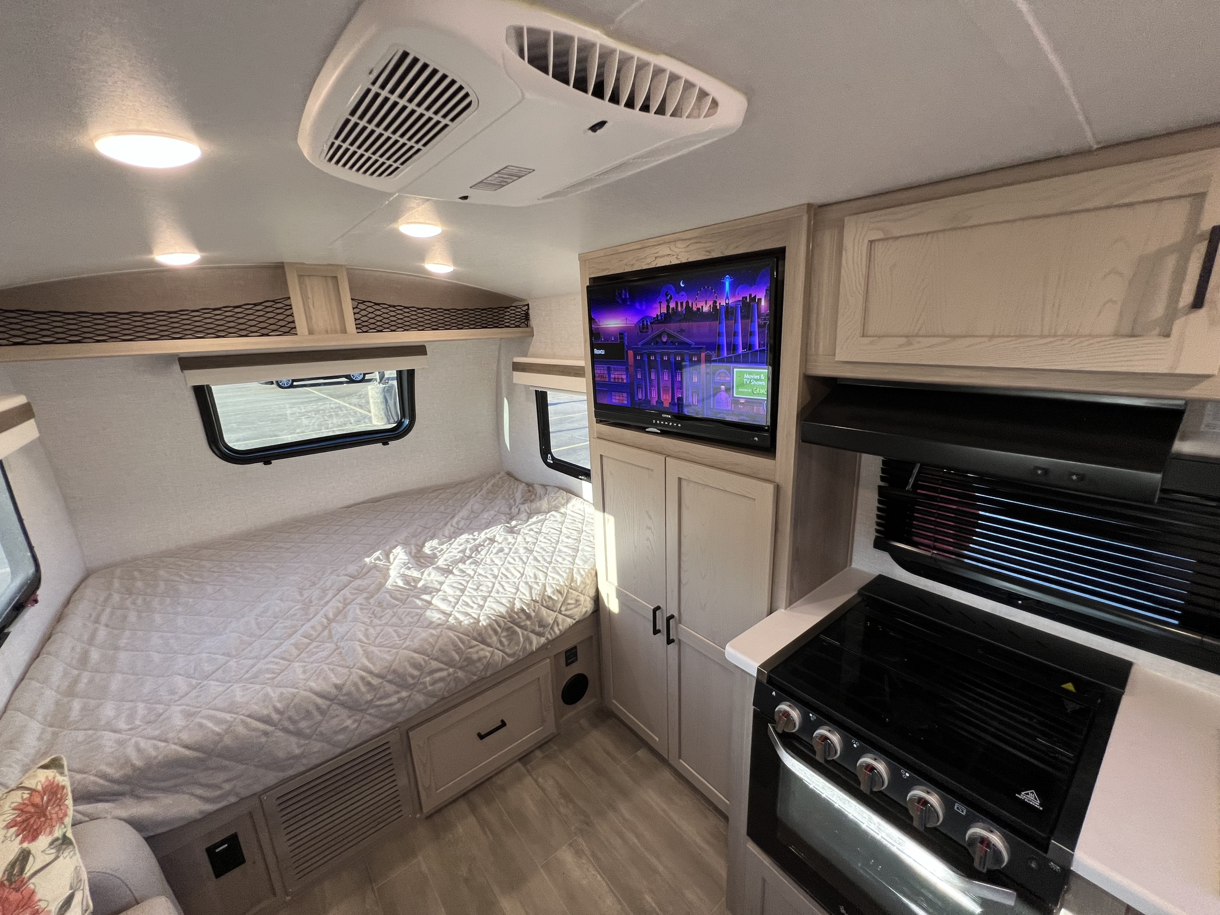 Explore this bright RV rental interior featuring a comfortable bed, flat-screen TV, and compact kitchen with stove.. Forest River Rockwood Geo Pro 2023