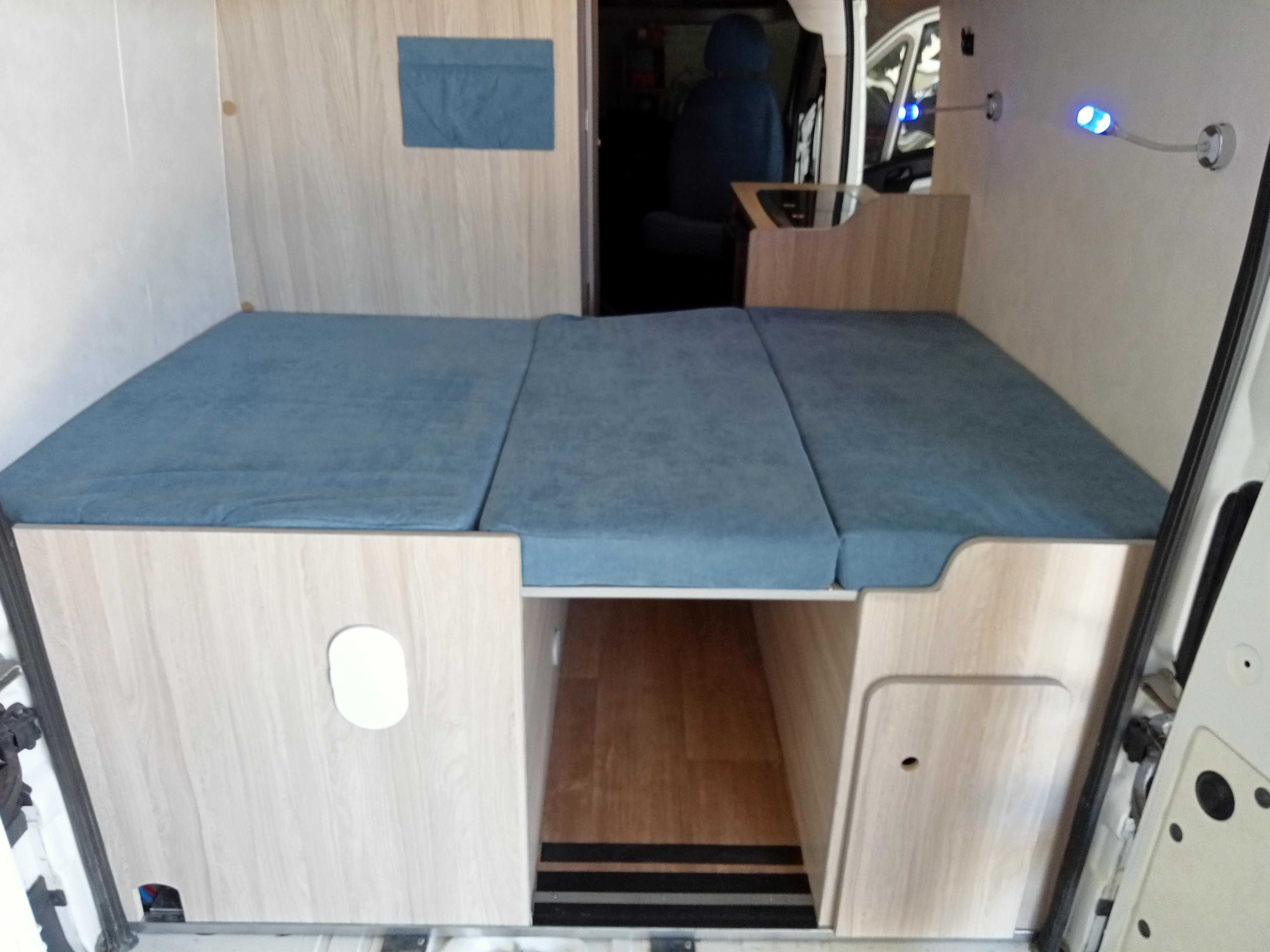 An RV rental's versatile interior with a blue modular bed, built-in storage, and functional lighting for adventure.. Fiat Ducato 2018