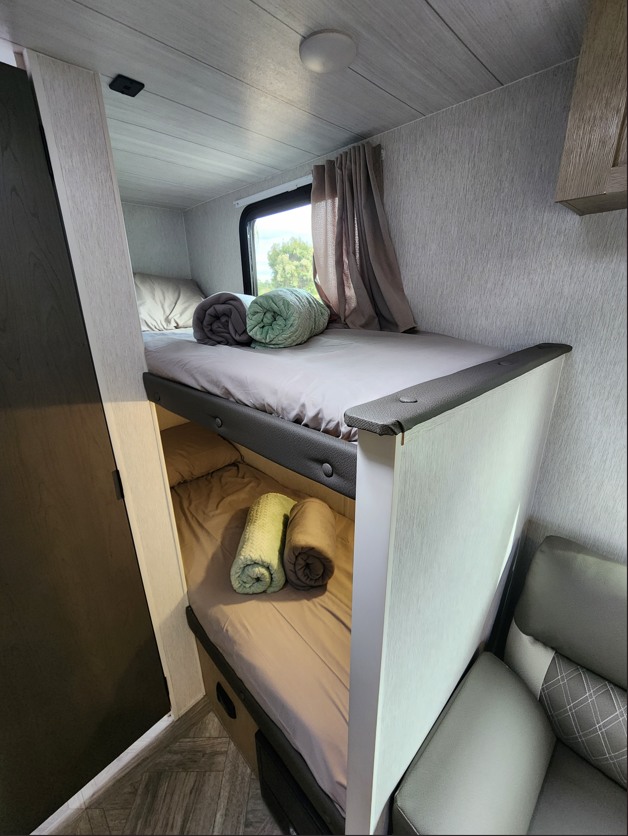 Cozy RV rental bunk beds: a neatly made interior sleeping area with two bunks, window, and rolled blankets.. Other Other 2024