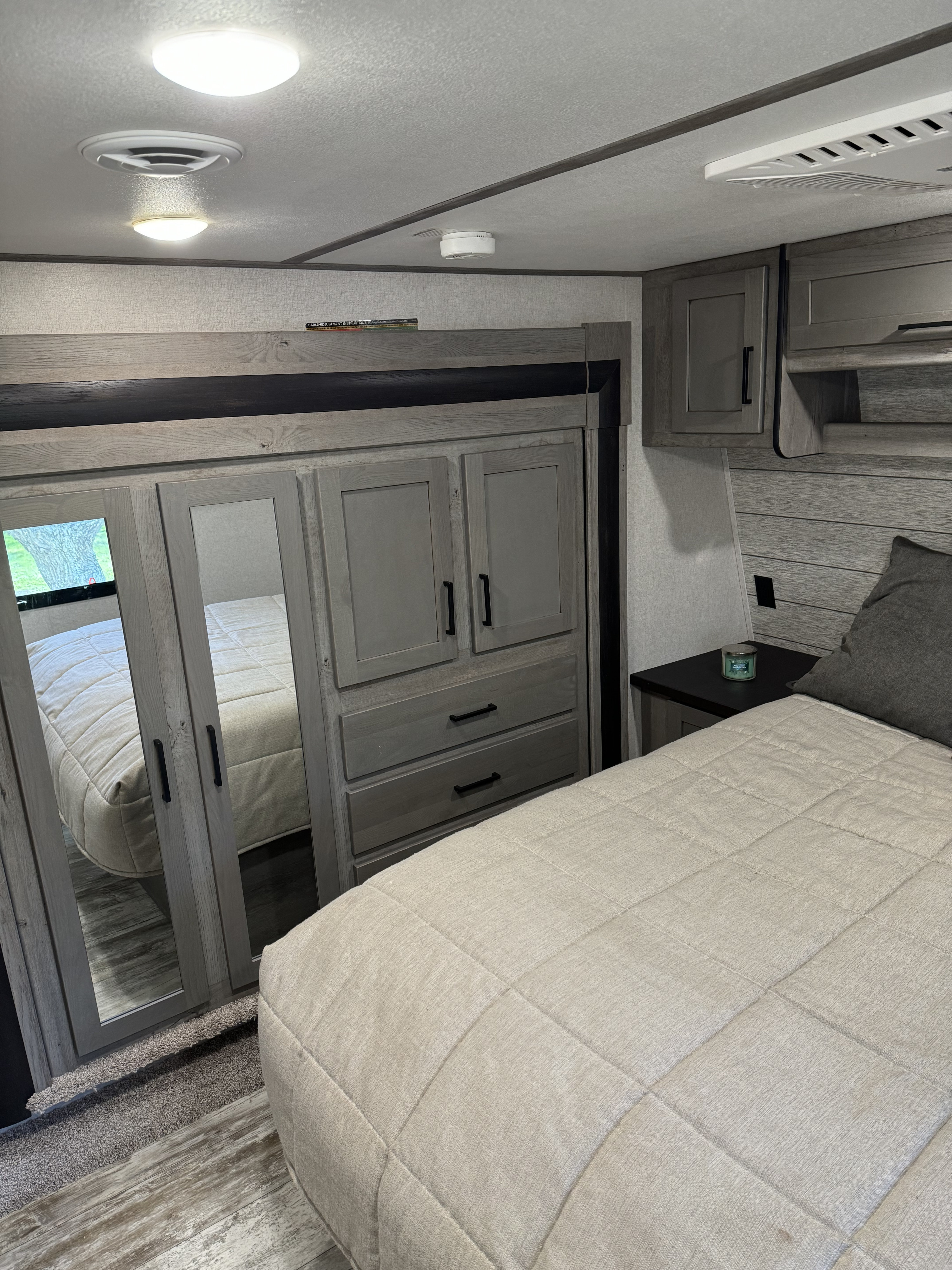 RV rental bedroom: a modern interior with a light quilted bed, mirrored wardrobe, nightstand, and overhead fixtures.. Keystone RV Carbon Toy Hauler 2021