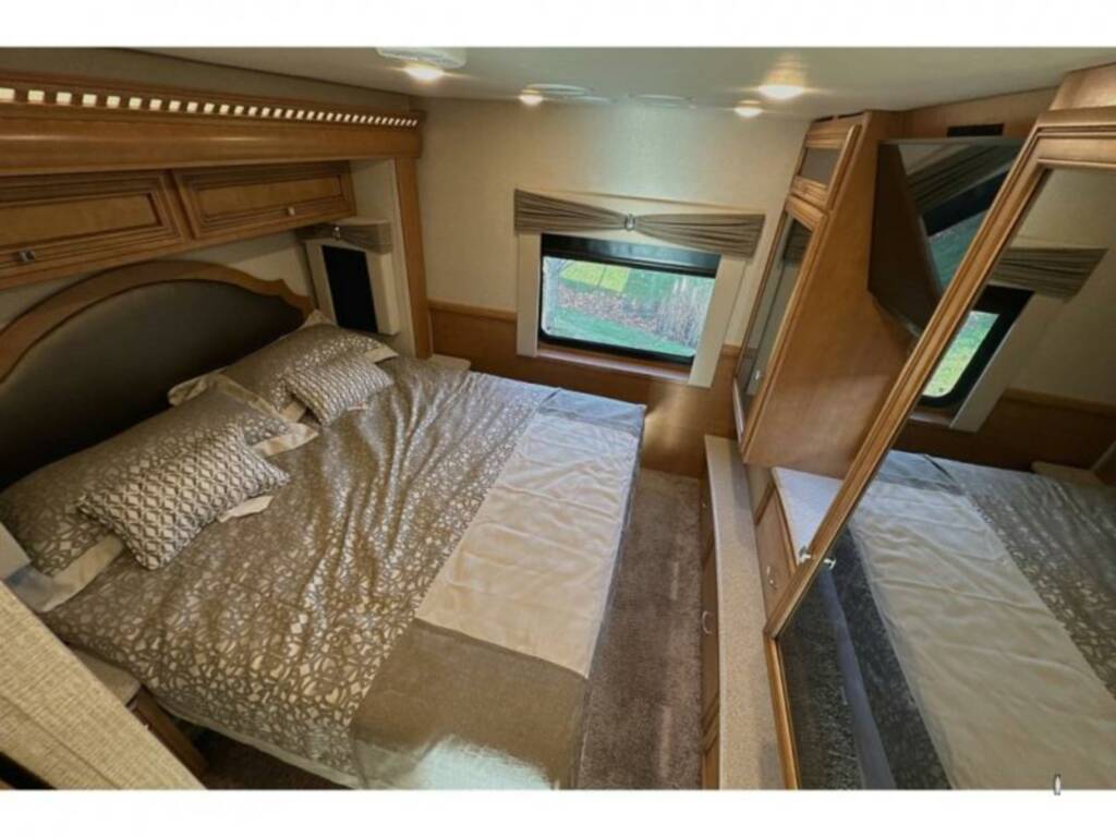 This RV rental features a comfortable bedroom with a large bed, decorative wood cabinetry, a window view, and mirrored storage.. Bay Star Bay Star Motorhome 2018