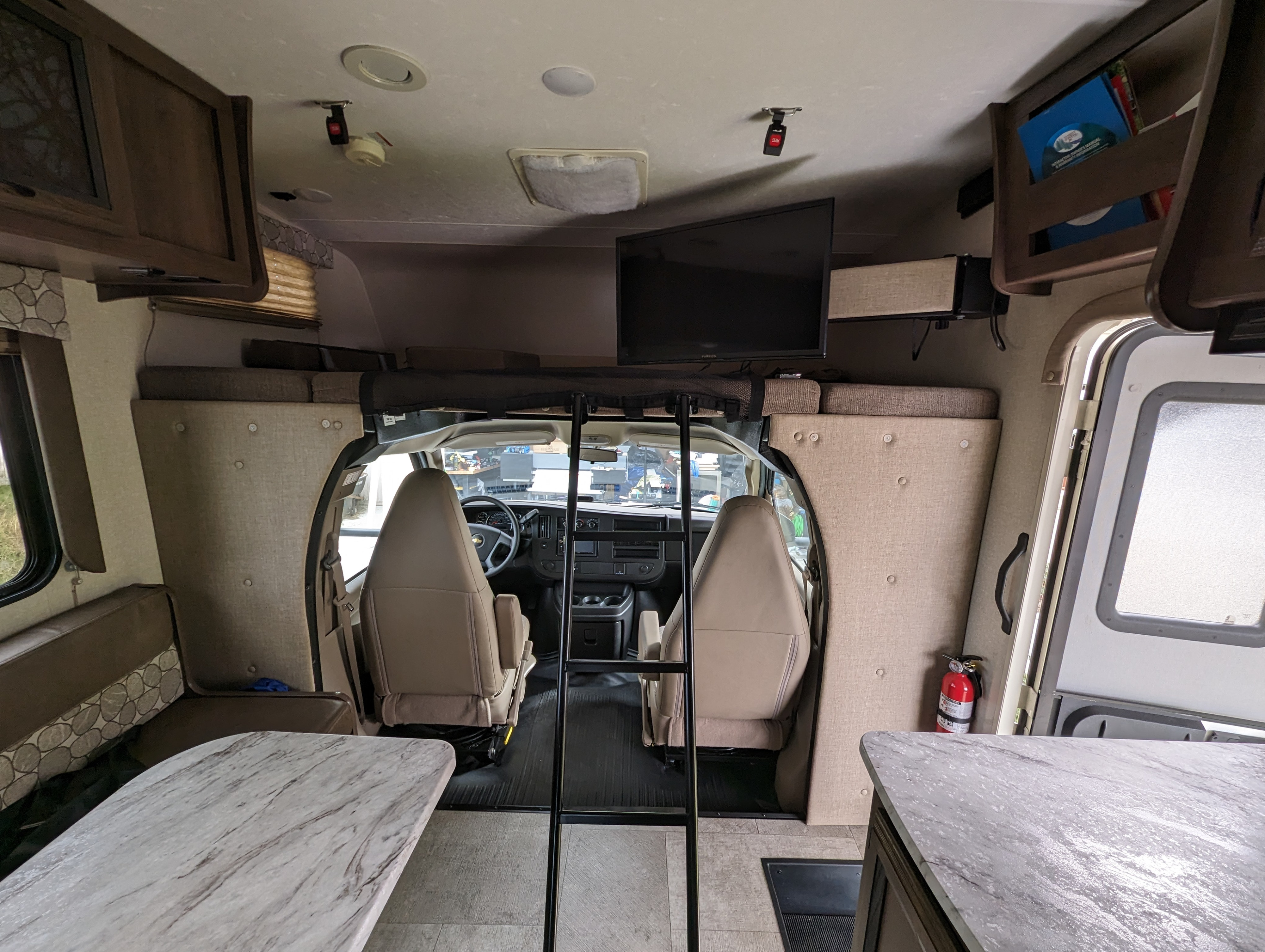 Interior of an **RV rental** showing the front cab, overhead bed with ladder, TV, storage, and a dining table setup.. Forest River Coachmen Freelander 2019