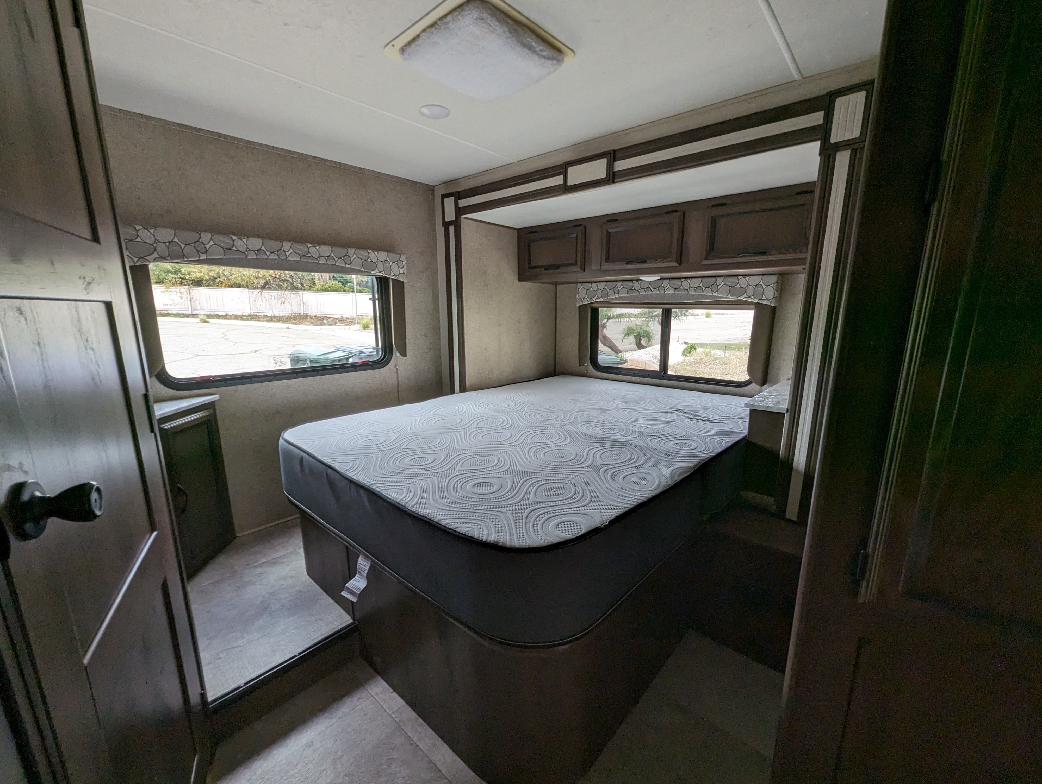 RV rental interior showing a cozy bedroom with a patterned mattress, overhead cabinets, and window views.. Forest River Coachmen Freelander 2019