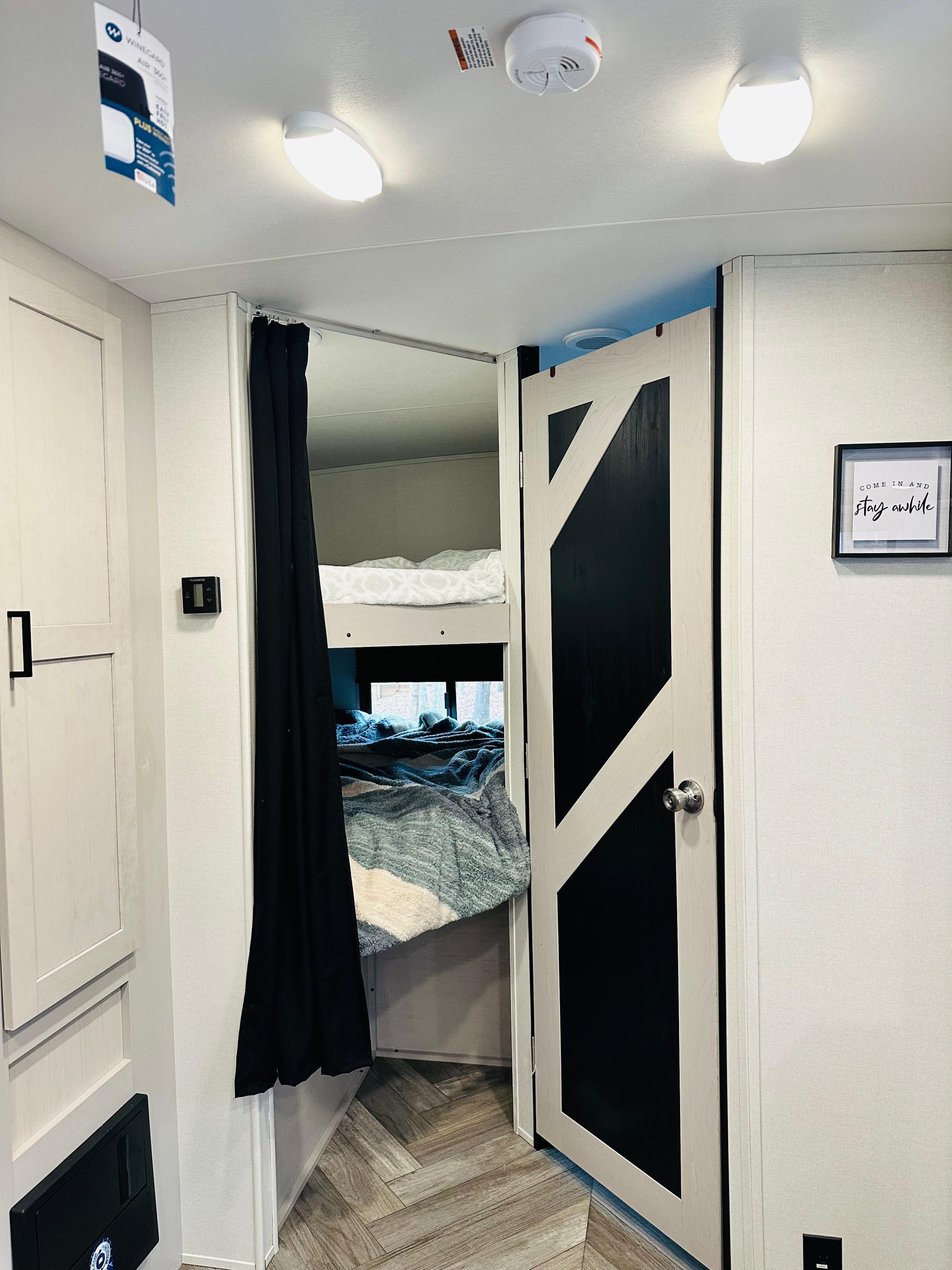 RV rental interior. Left: Bunk beds with black privacy curtain. Right: Modern black/wood barn door. Cozy, compact living space.. Heartland RVs Mallard 2024
