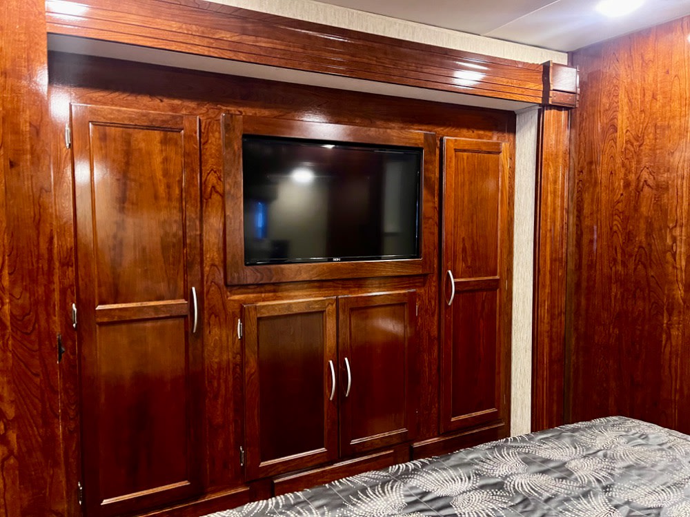 Cozy RV rental bedroom featuring rich wooden cabinetry, an integrated TV, and comfortable bedding.. Coachmen Mirada 2018