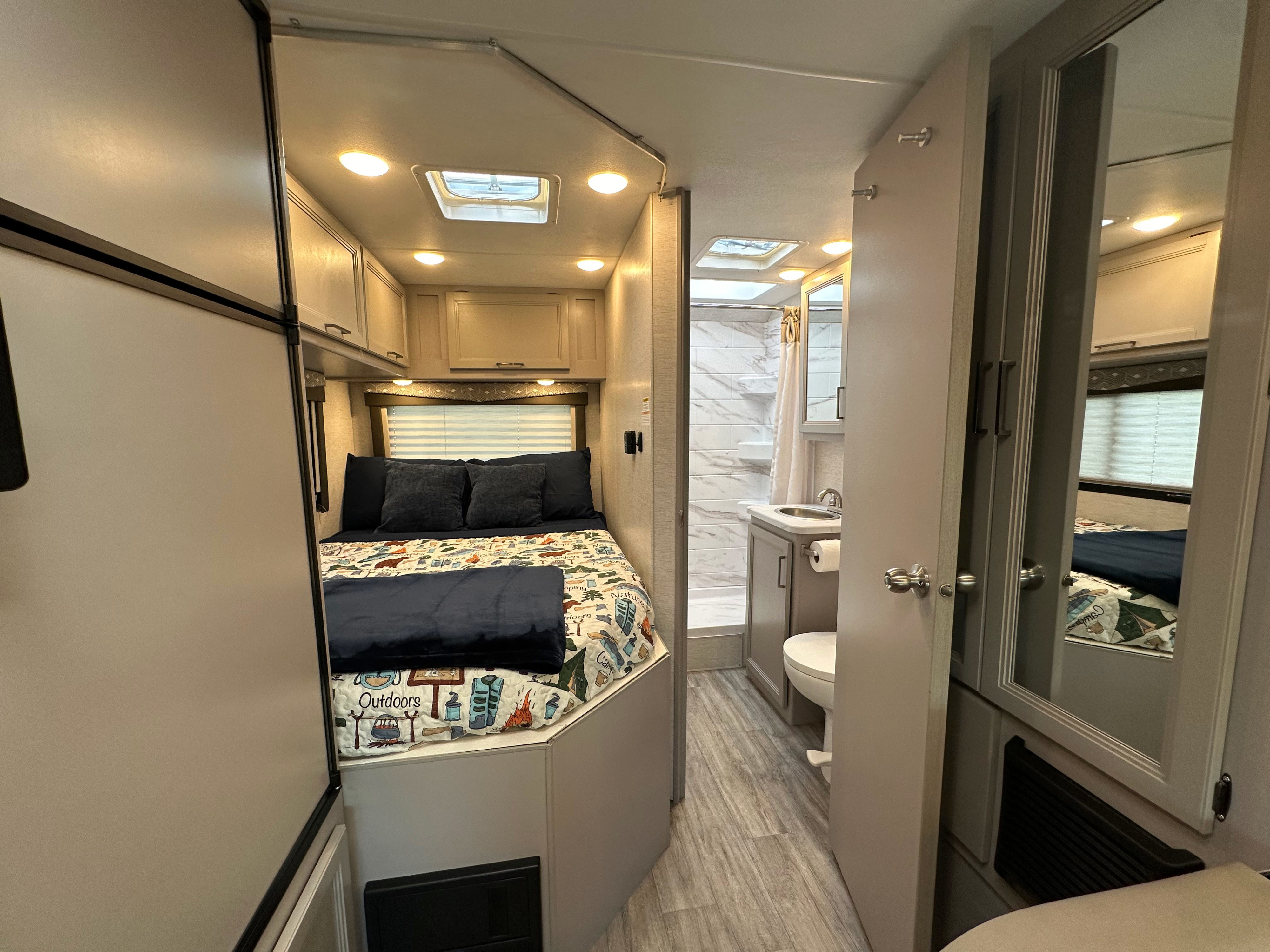RV rental interior: cozy bedroom with camping-themed quilt & storage, compact bathroom, and wood-look flooring.. Thor Four Winds 2024