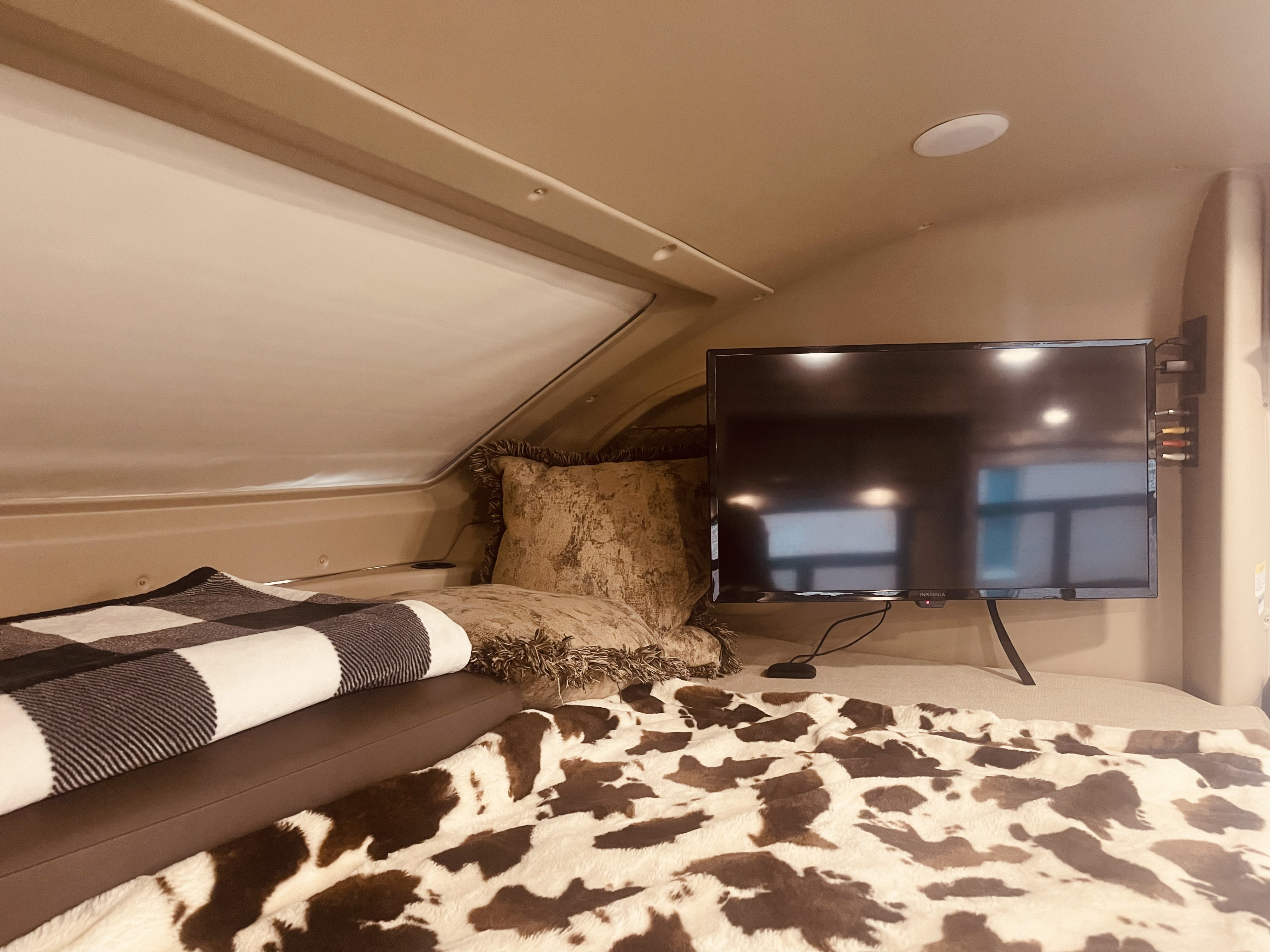 Cozy RV rental interior with bed, cow print blanket, pillows, TV, and an overhead window.. Entegra Coach Odyssey 2020