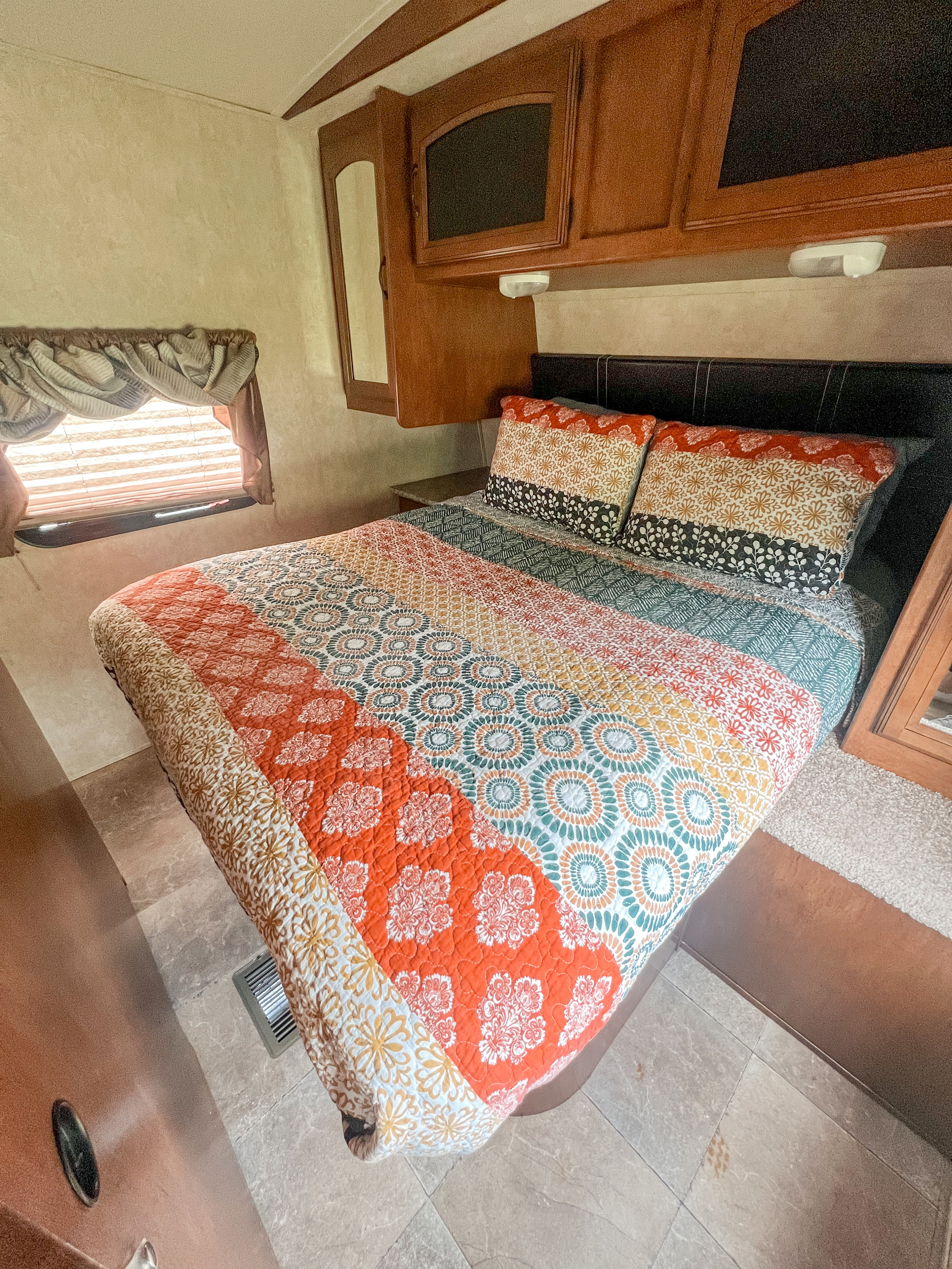Cozy RV rental bedroom with a vibrant patterned quilt, overhead cabinets, and a window for natural light.. Forest River Wildwood Heritage Glen Lite 2013