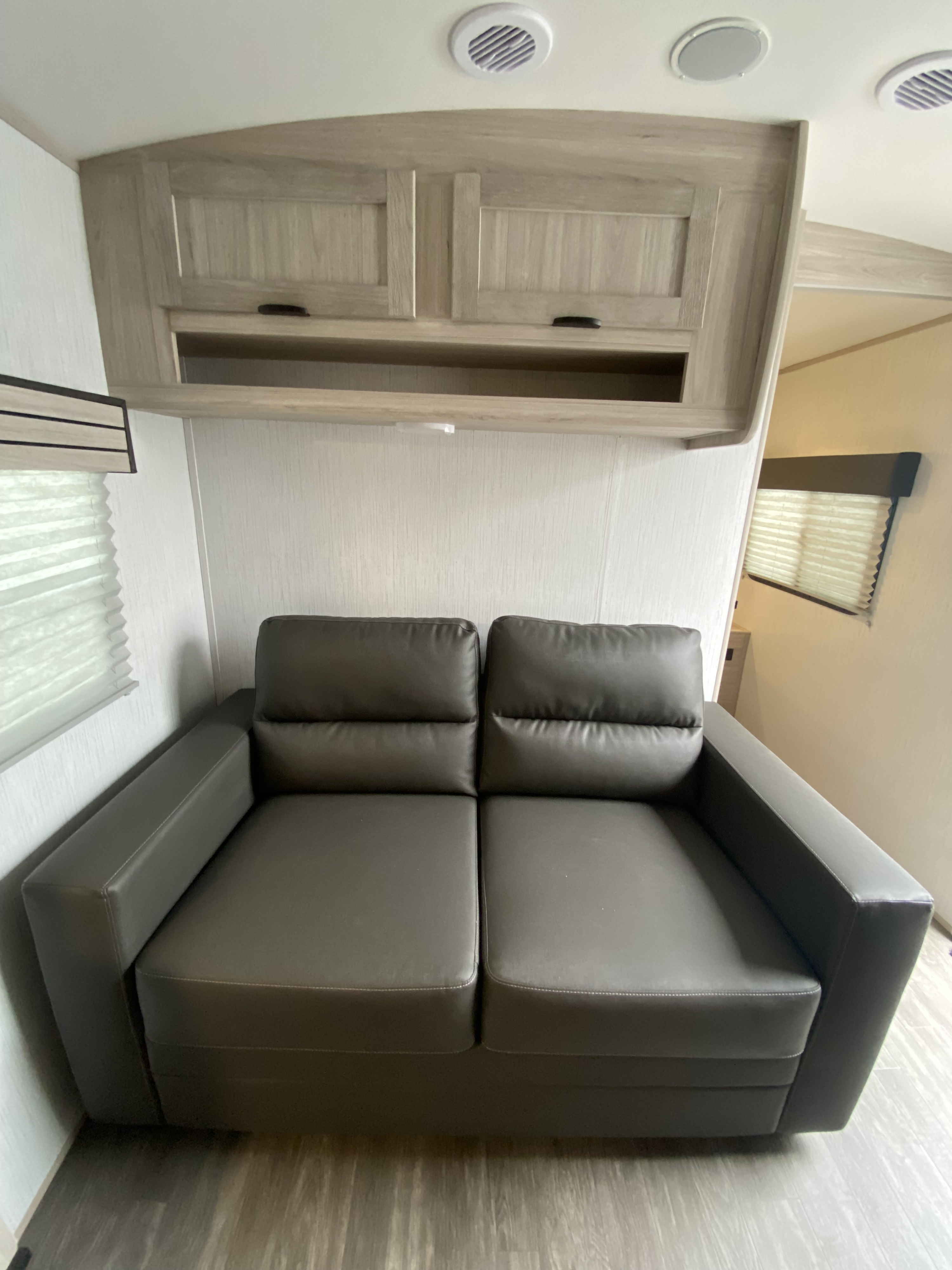This RV rental offers a compact and comfortable living space featuring a dark sofa, overhead cabinets, and window blinds.. Cruiser RV Shadow Cruiser 2022