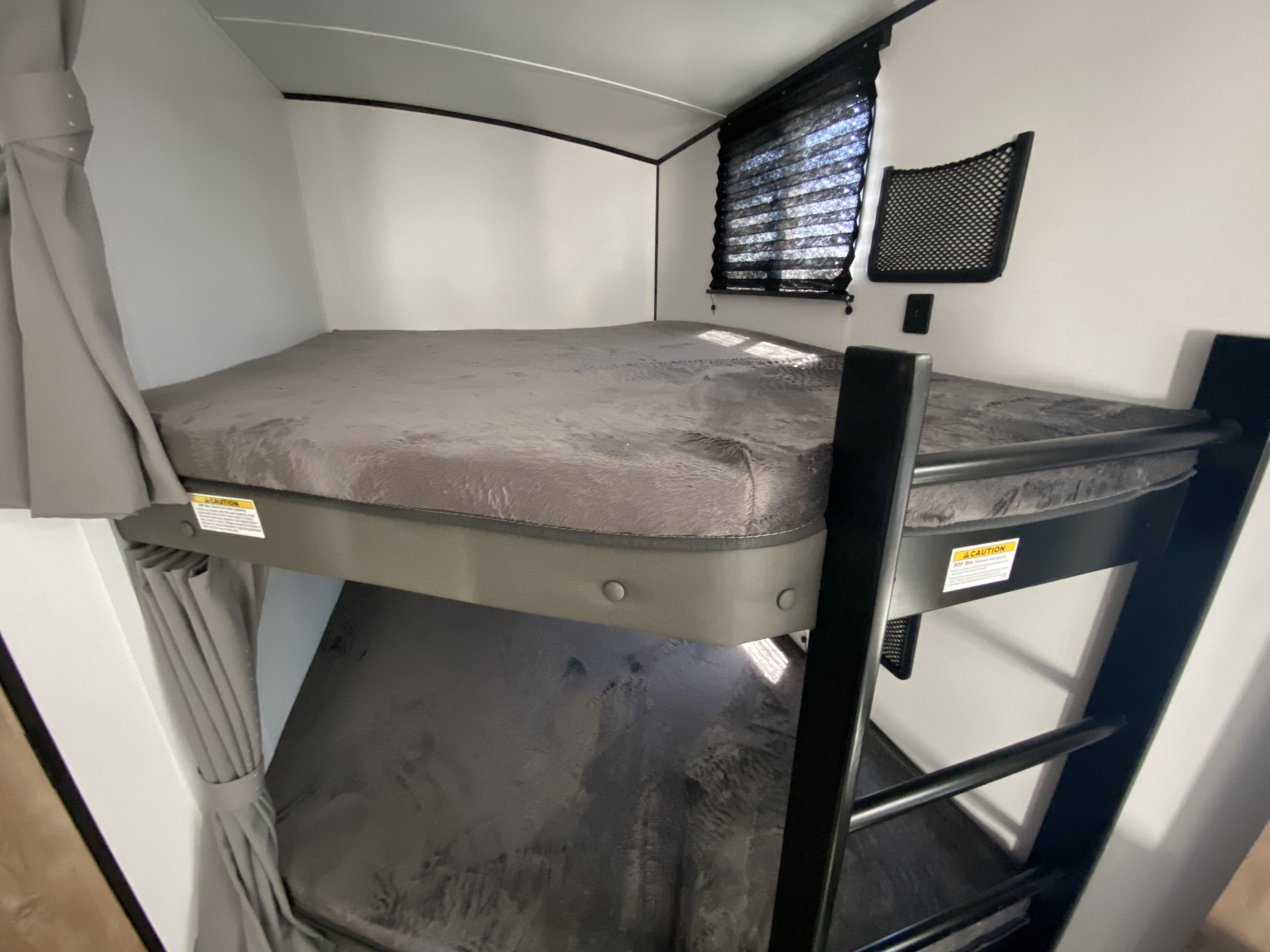 RV rental interior features comfortable bunk beds, a window with blinds, and storage netting for travel.. Keystone RV Springdale 2022