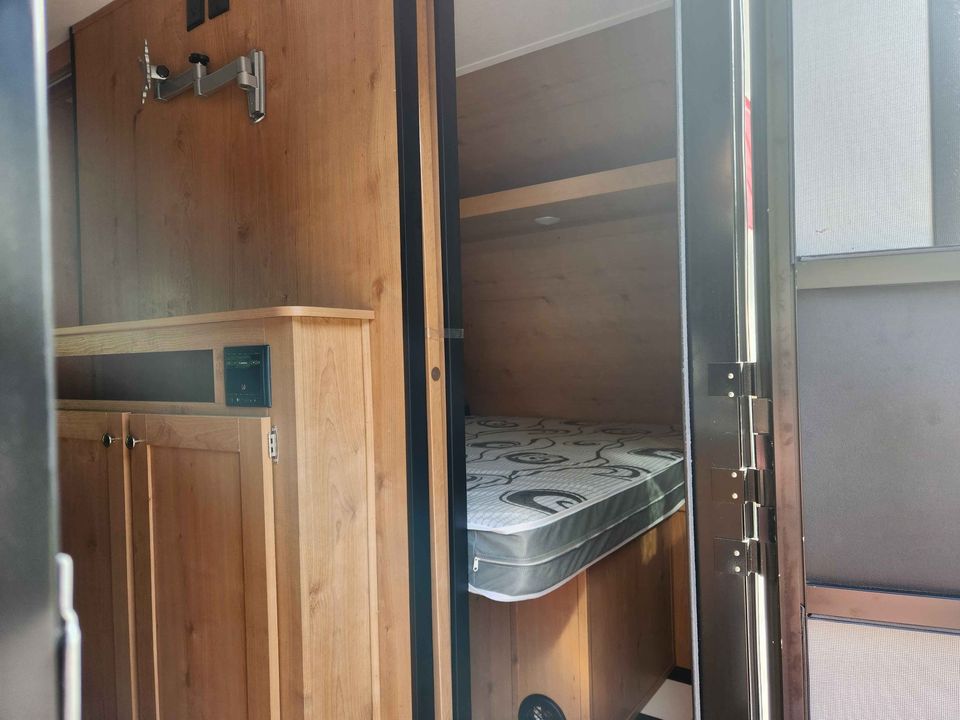 Cozy RV rental interior featuring a comfortable bed, storage cabinet, and TV mount for your travel comfort.. Riverside Rv Retro 2023