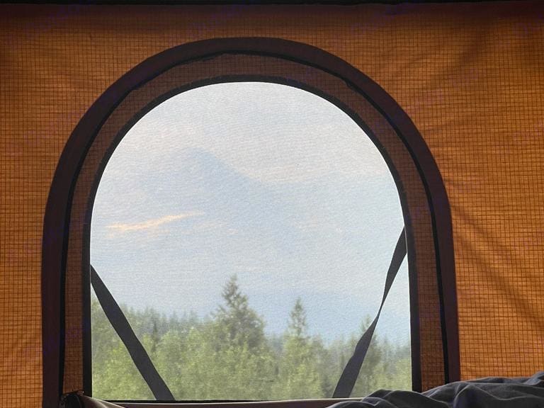 Inside an RV rental, an arched mesh window frames a distant mountain over a lush forest. Cozy camping view.. NISSAN XTERRA 2007