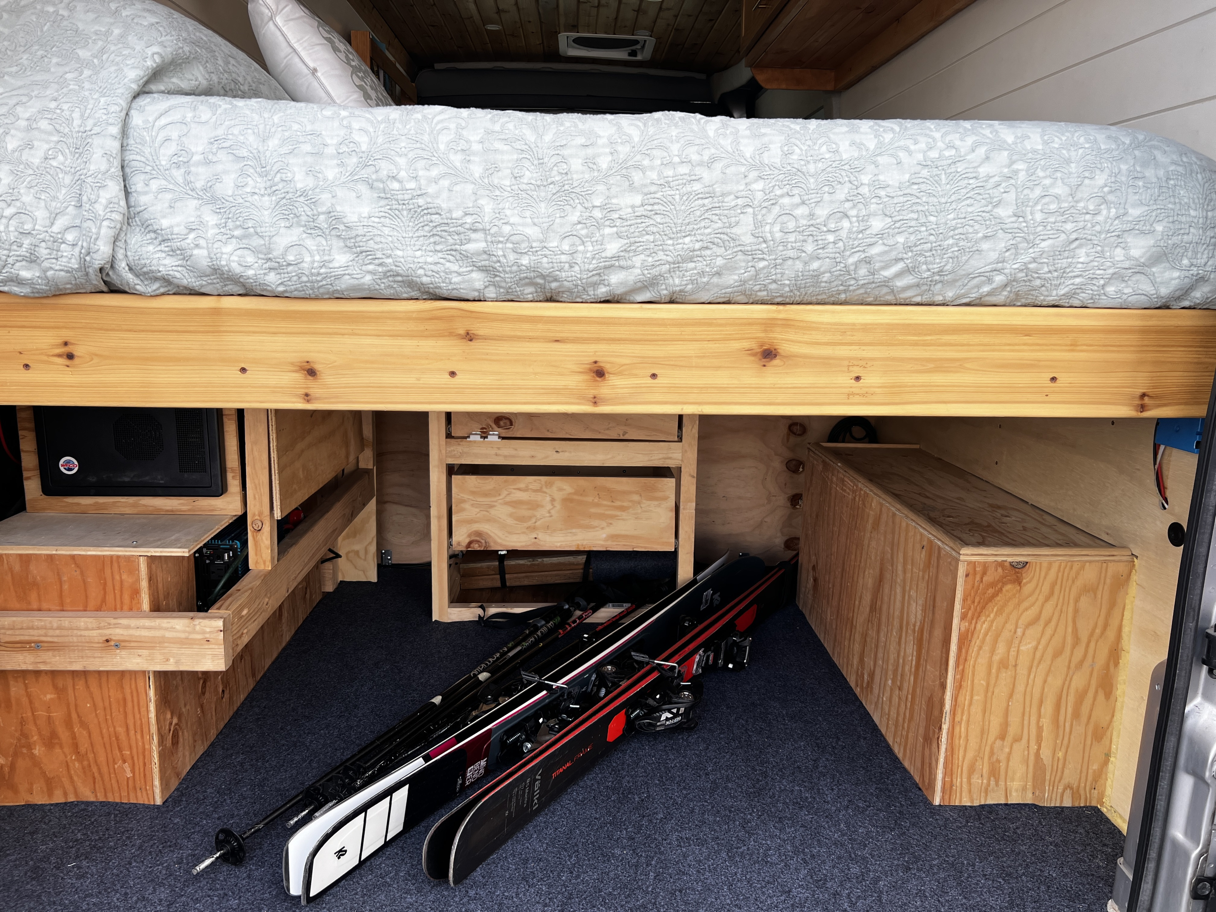 RV rental interior with an elevated bed, custom storage compartments, and skis on the carpeted floor, ready for adventure.. Ram Promaster 2019