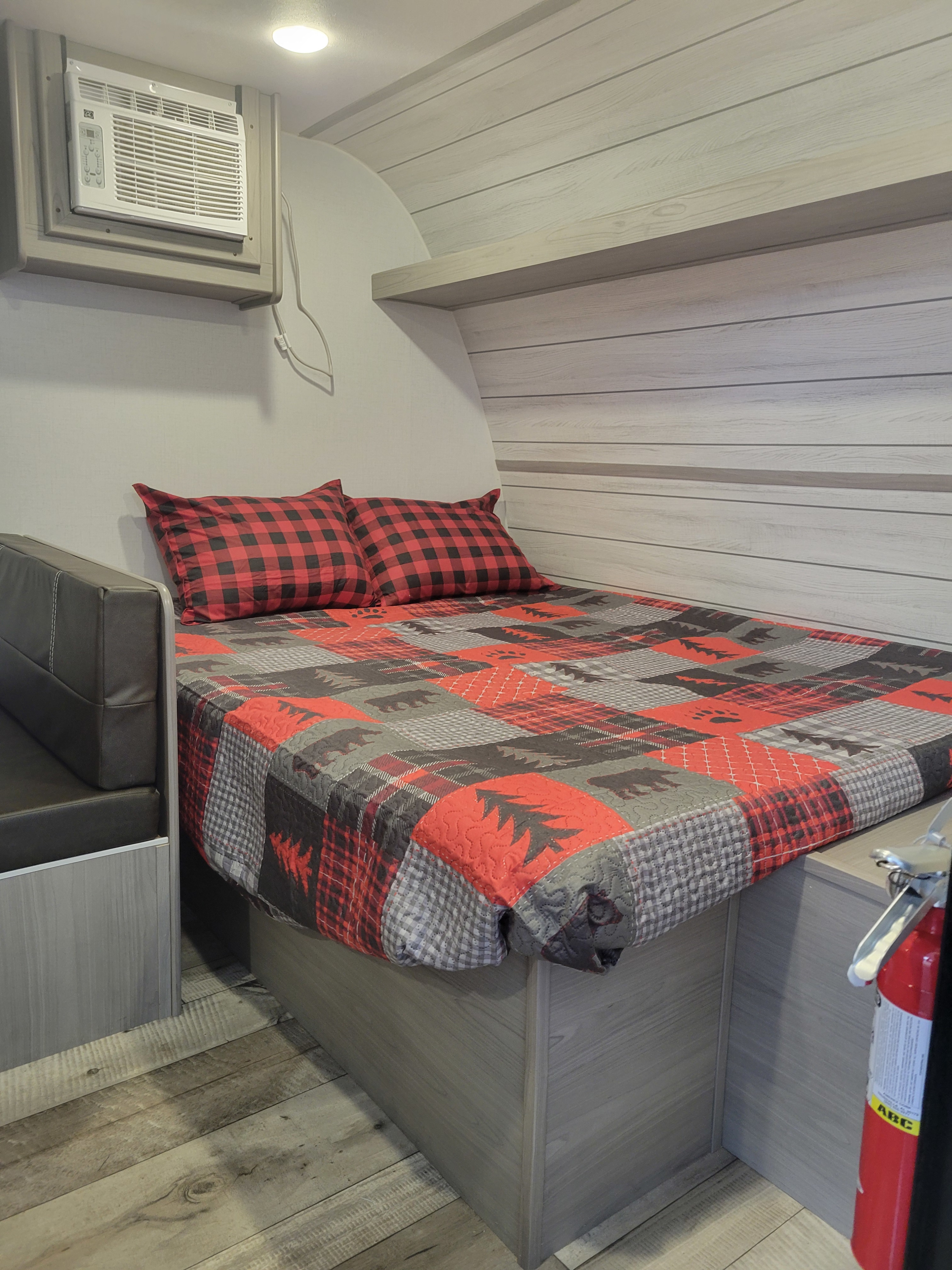 This RV rental offers a compact sleeping area with a cozy plaid quilt, bench seating, and a wall-mounted AC unit.. Coleman Coleman Lantern 17B 2024