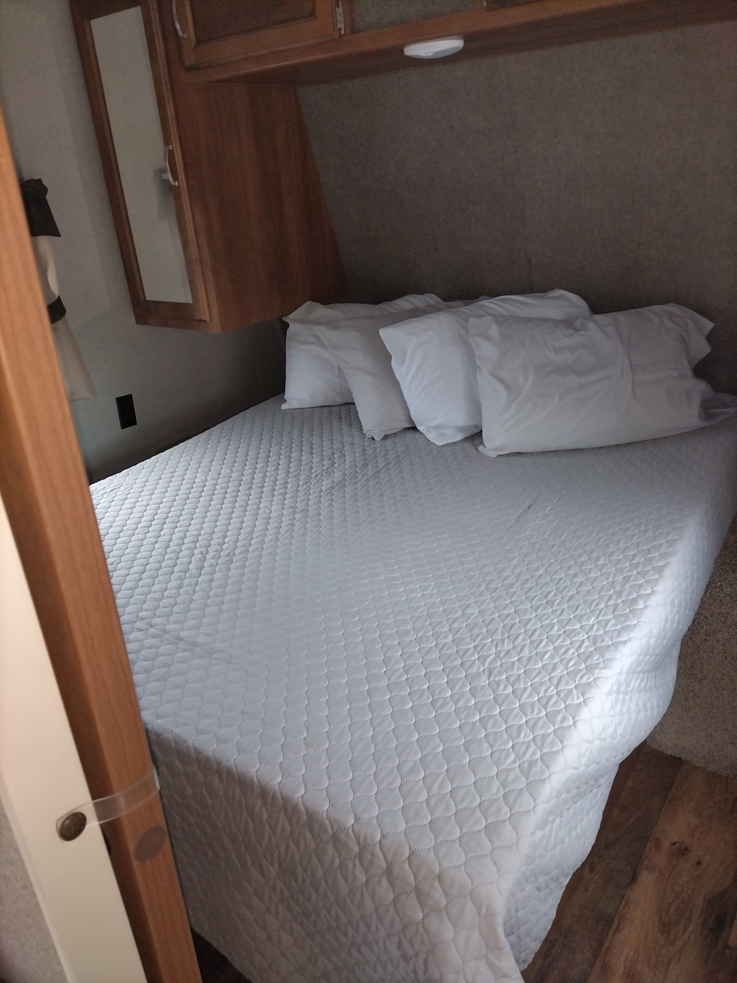 Compact RV rental bedroom featuring a clean white quilted bed, pillows, wood cabinets, & mirror.. Keystone RV Springdale Eco-Lite 2018