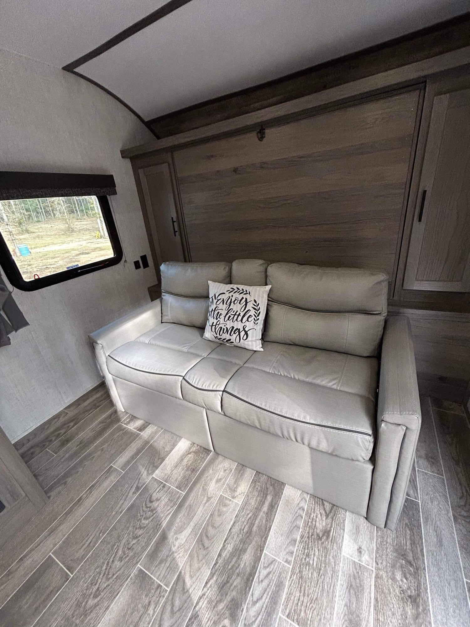 Comfortable RV rental interior with a gray sofa, wood-look floor, and a large window view.. Gulf Stream Ameri-Lite 2022