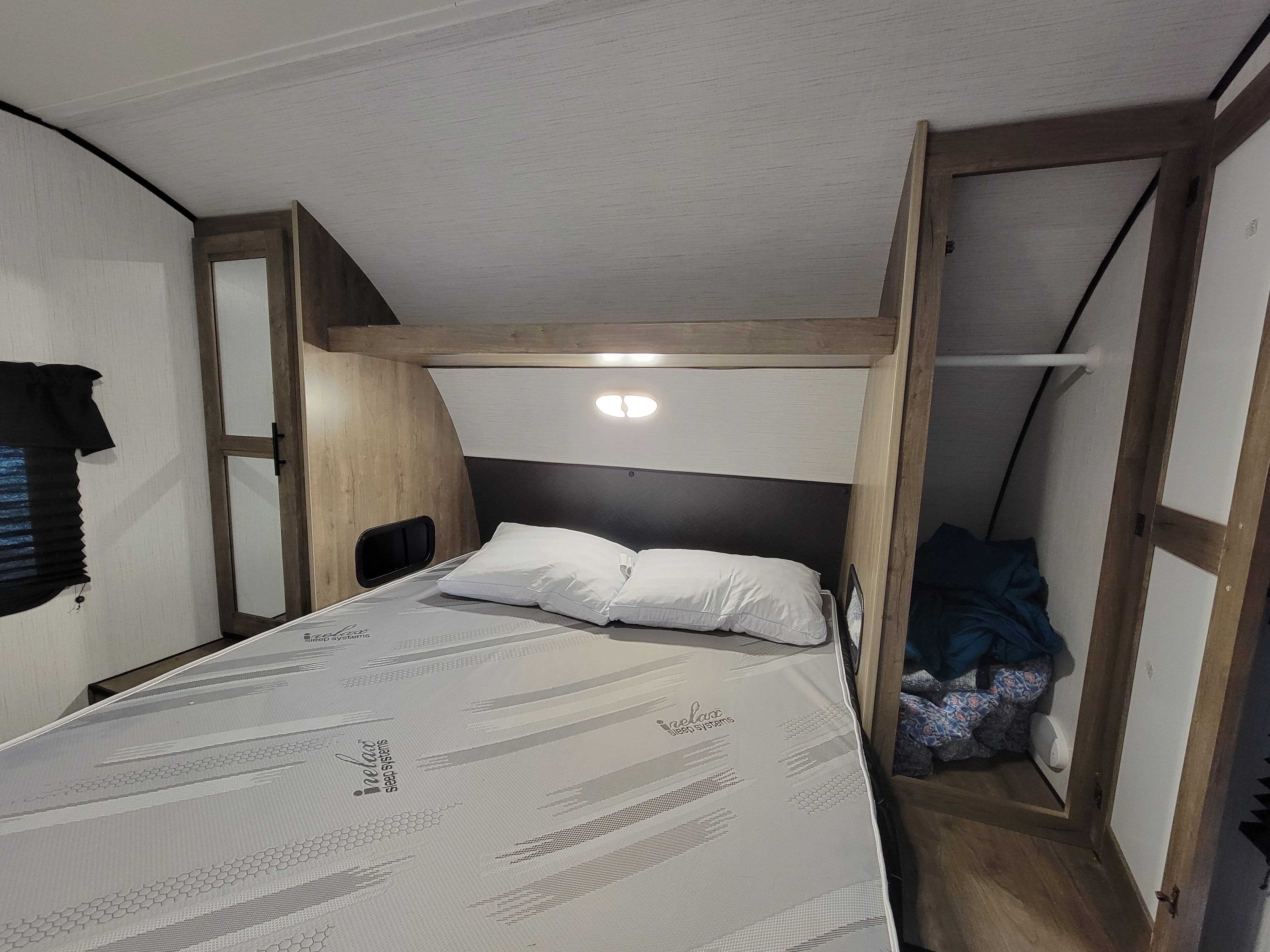 This RV rental bedroom features a comfortable bed with pillows, built-in overhead light, and convenient closet storage.. Heartland RVs Pioneer 2022
