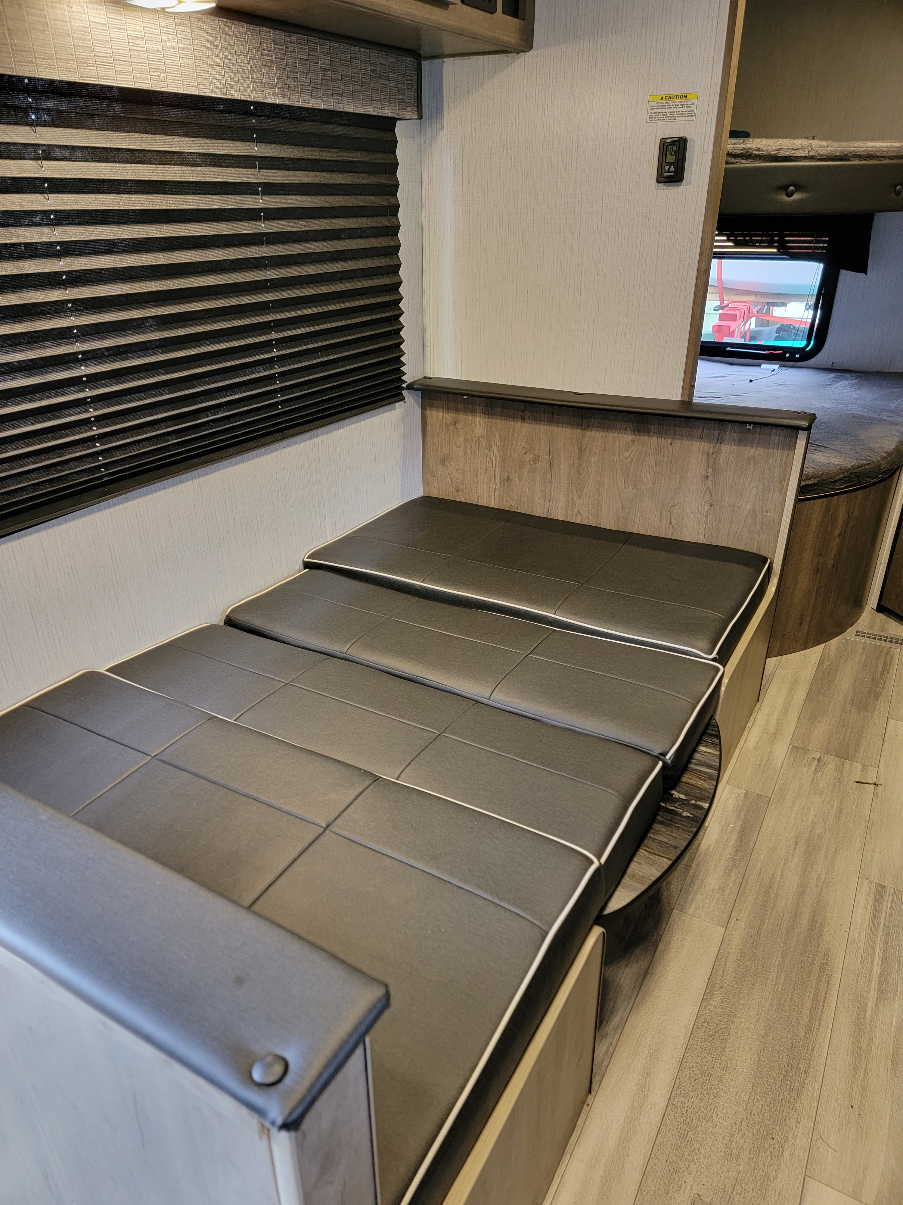 Inside this RV rental: a flexible dark grey convertible dinette/bed area, window blinds, and bunk beds visible in the background.. Heartland RVs Pioneer 2022