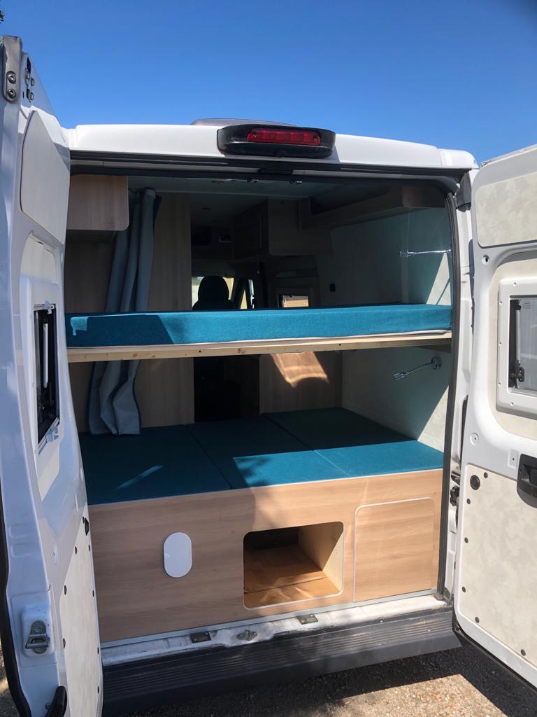 RV rental interior: two-tier bunk beds with blue cushions and wood cabinetry. Ideal camper van for adventures.. Fiat Ducato 2018