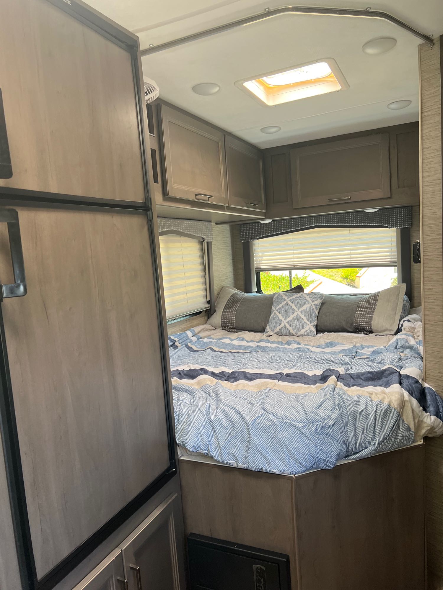 Cozy RV rental interior: a well-lit bedroom with a blue patterned comforter and pillows, adjacent to a refrigerator.. Thor Chateau 2023
