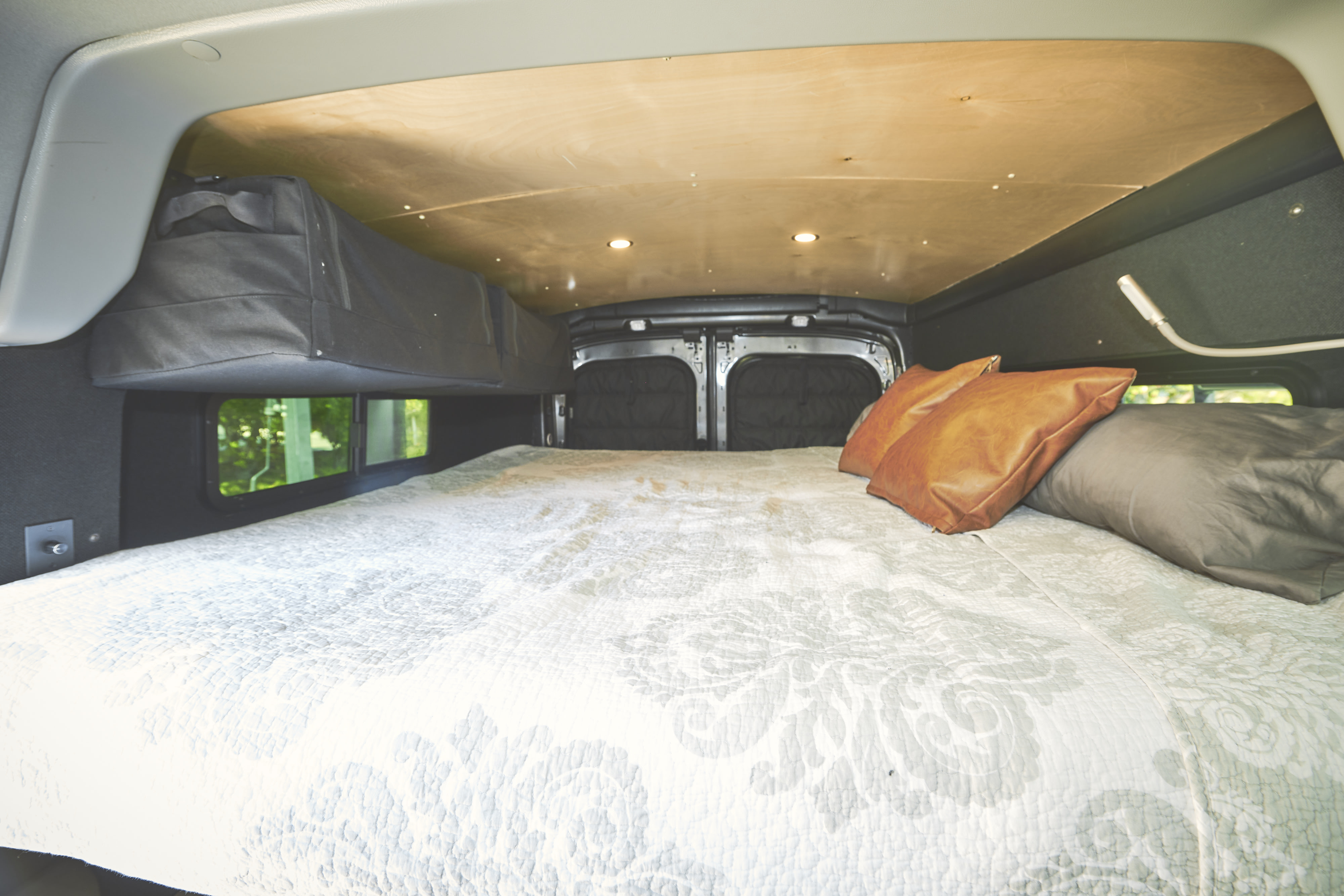 Cozy RV rental camper van interior with a large bed, patterned quilt, leather and fabric pillows, and overhead storage.. Ford Transit 2020