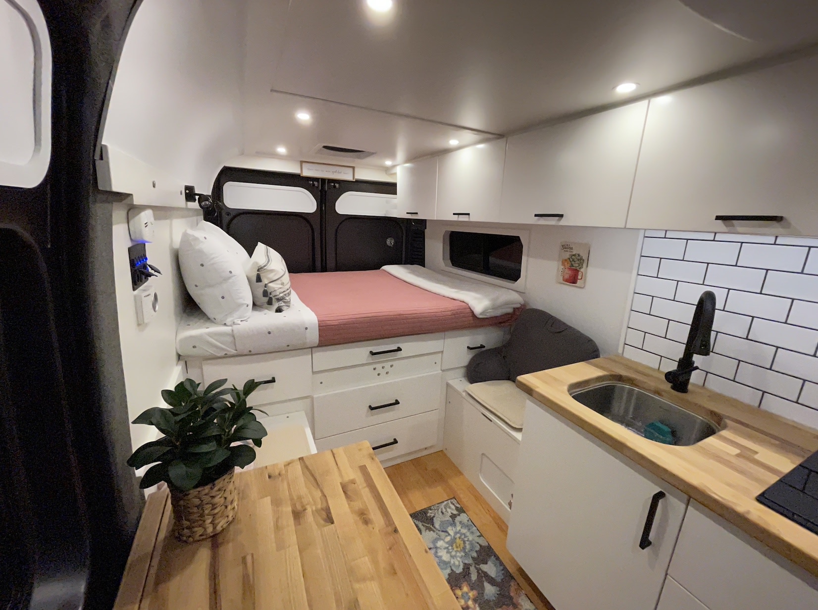 Explore this compact RV rental interior with a cozy bed, sleek kitchen, white cabinets, and clever storage solutions.. Dodge RAM ProMaster High Roof 2021