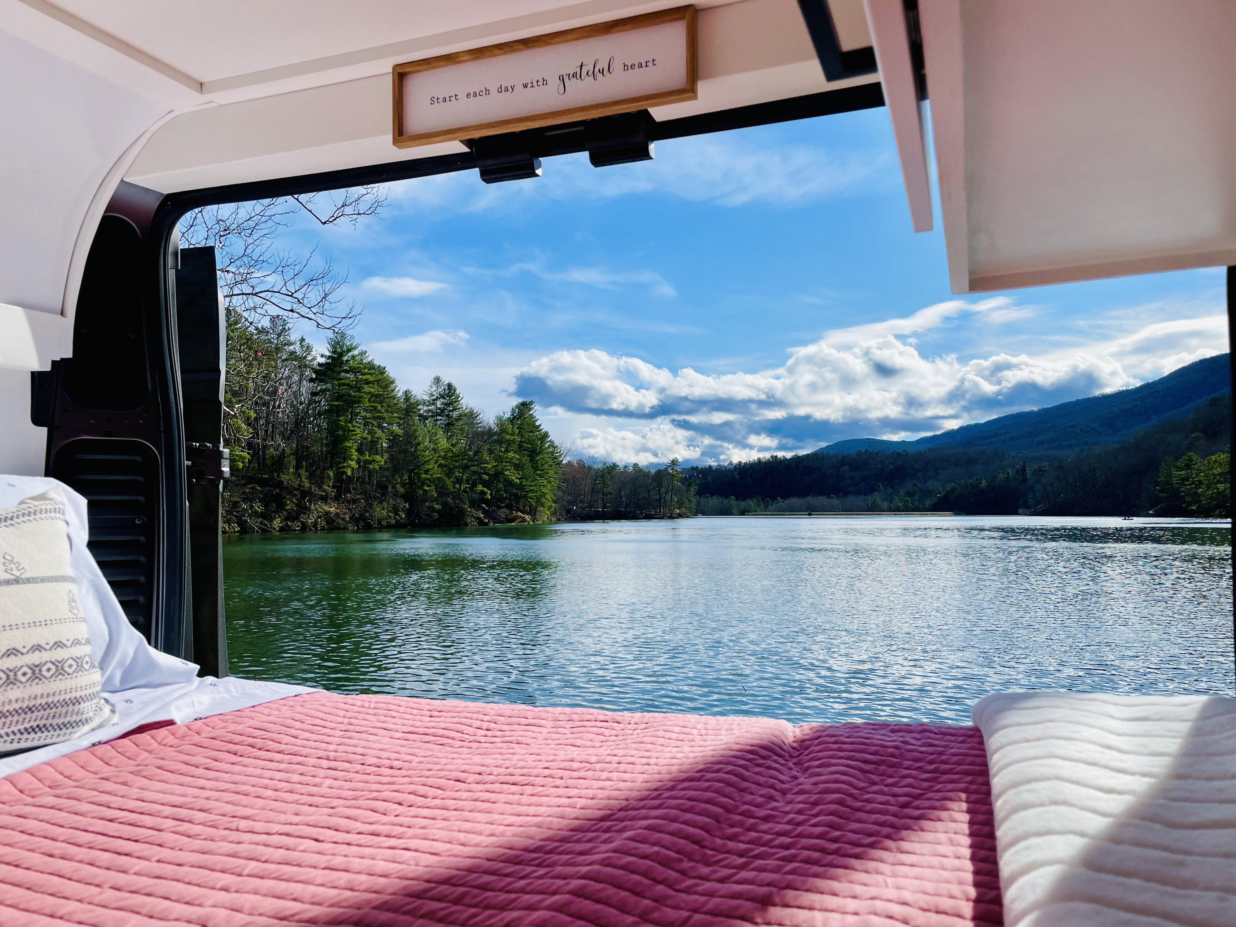 Cozy RV rental bed with an expansive view of a serene lake, lush trees, and majestic mountains. Embrace van life.. Dodge RAM ProMaster High Roof 2021