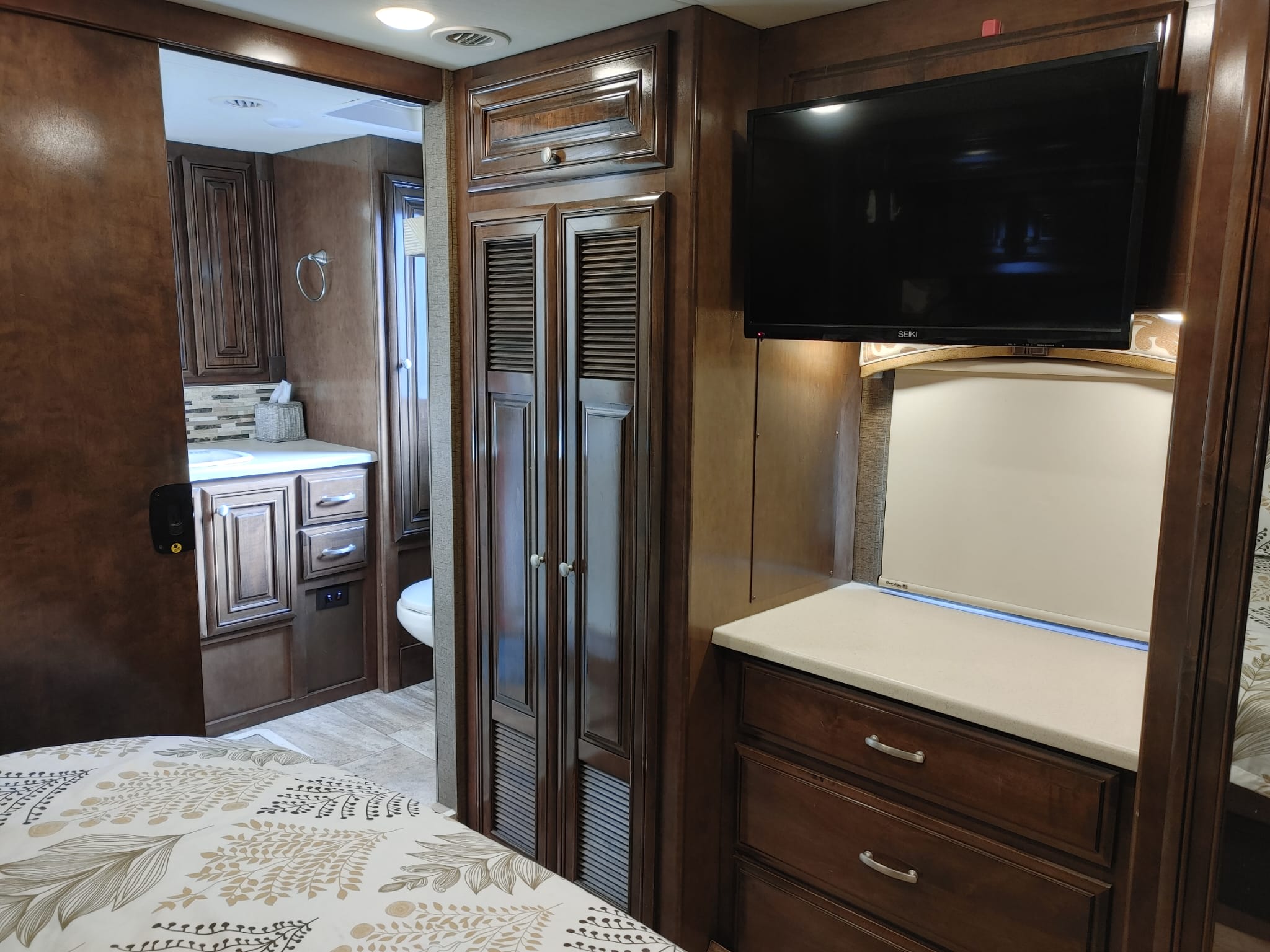 This inviting rv rental features a cozy bedroom with patterned bedding, TV, wood cabinets, and a visible attached bathroom.. Thor Palazzo 2017