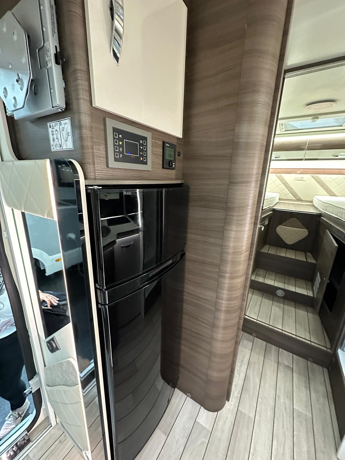 Compact RV rental interior featuring a black refrigerator, control panels, and a cozy sleeping area with steps.. McLouis Yearling 83 2024