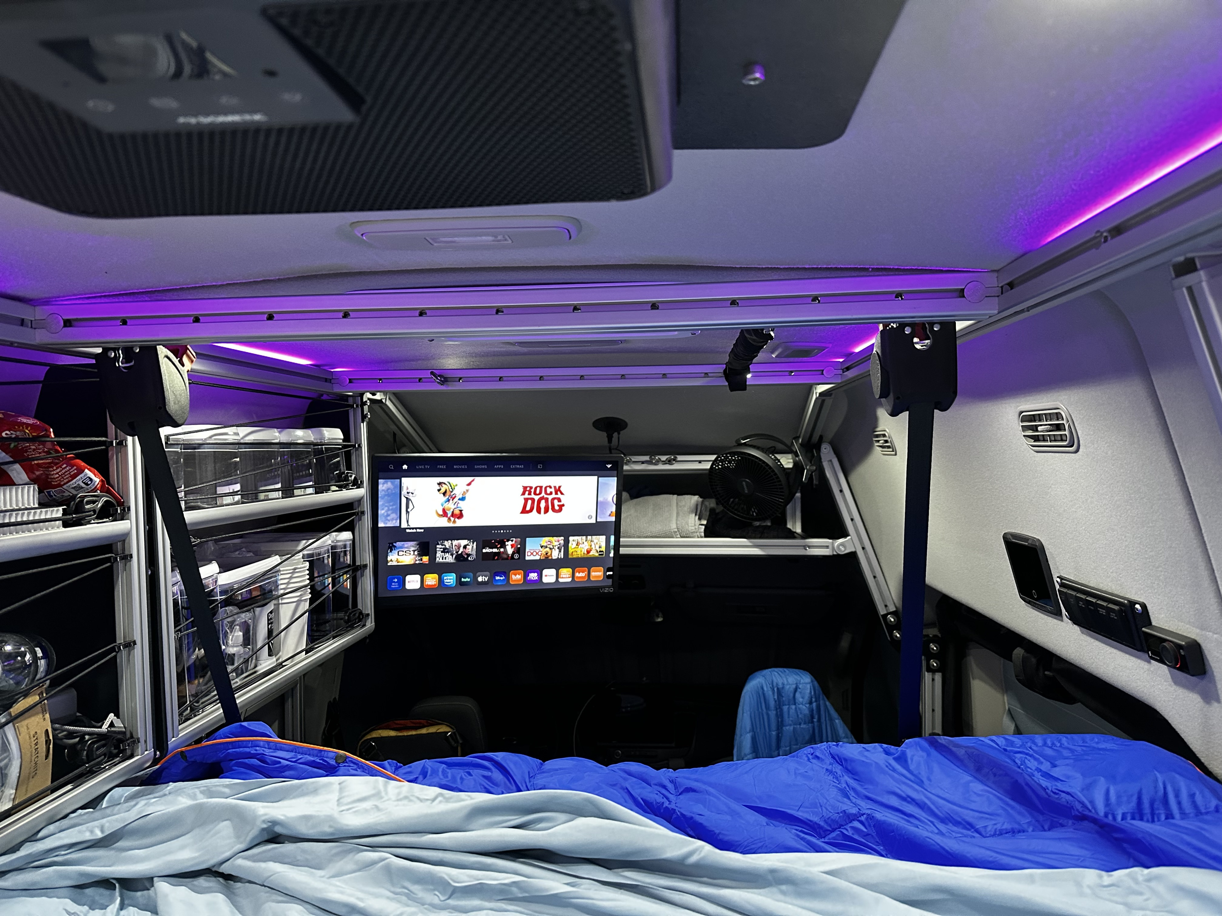Inside a modern rv rental: a cozy bed, Vizio TV for entertainment, organized overhead storage, and ambient purple lighting.. Vandoit DO 2023