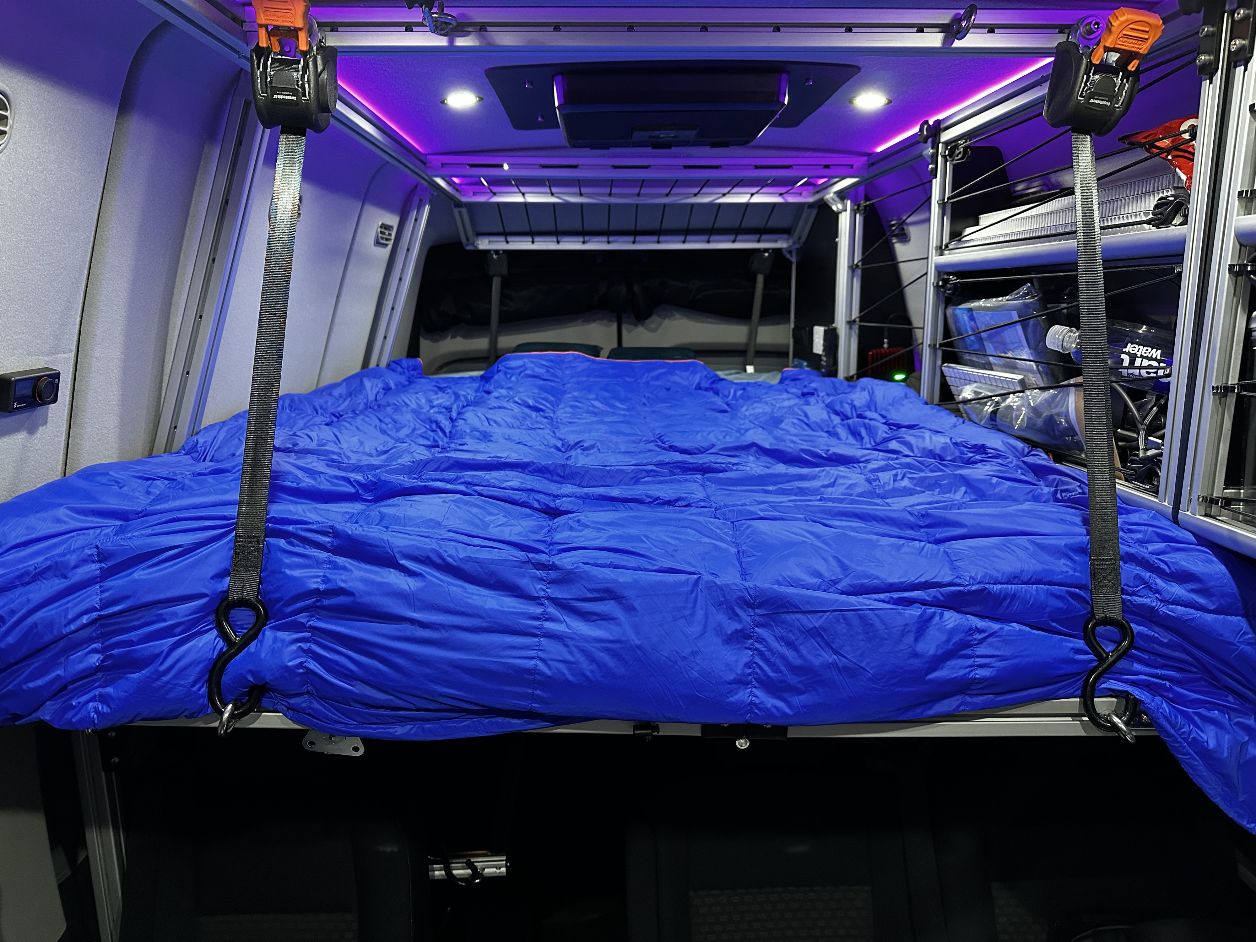 This RV rental interior offers a comfortable blue sleeping setup on a raised platform, with ambient lighting and organized storage.. Vandoit DO 2023