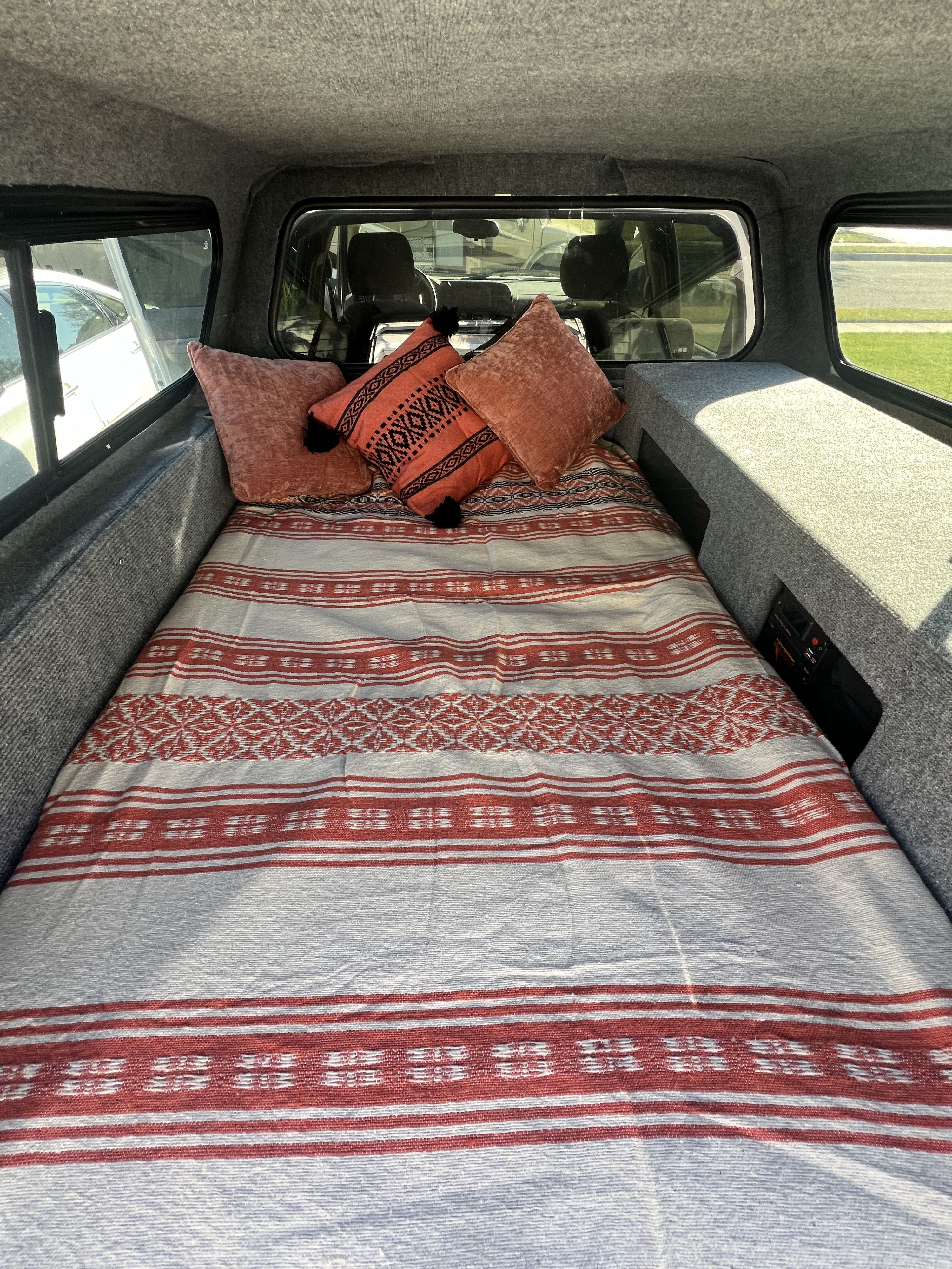 Cozy truck camper interior with a bed, red blanket, pillows, and built-in storage. Ideal for RV rental road trips.. Chevrolet Silverado 1500 2009
