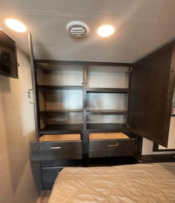 This RV rental bedroom features clever dark wood built-in storage with open shelves and pull-out drawers.. Jayco Alante 2021