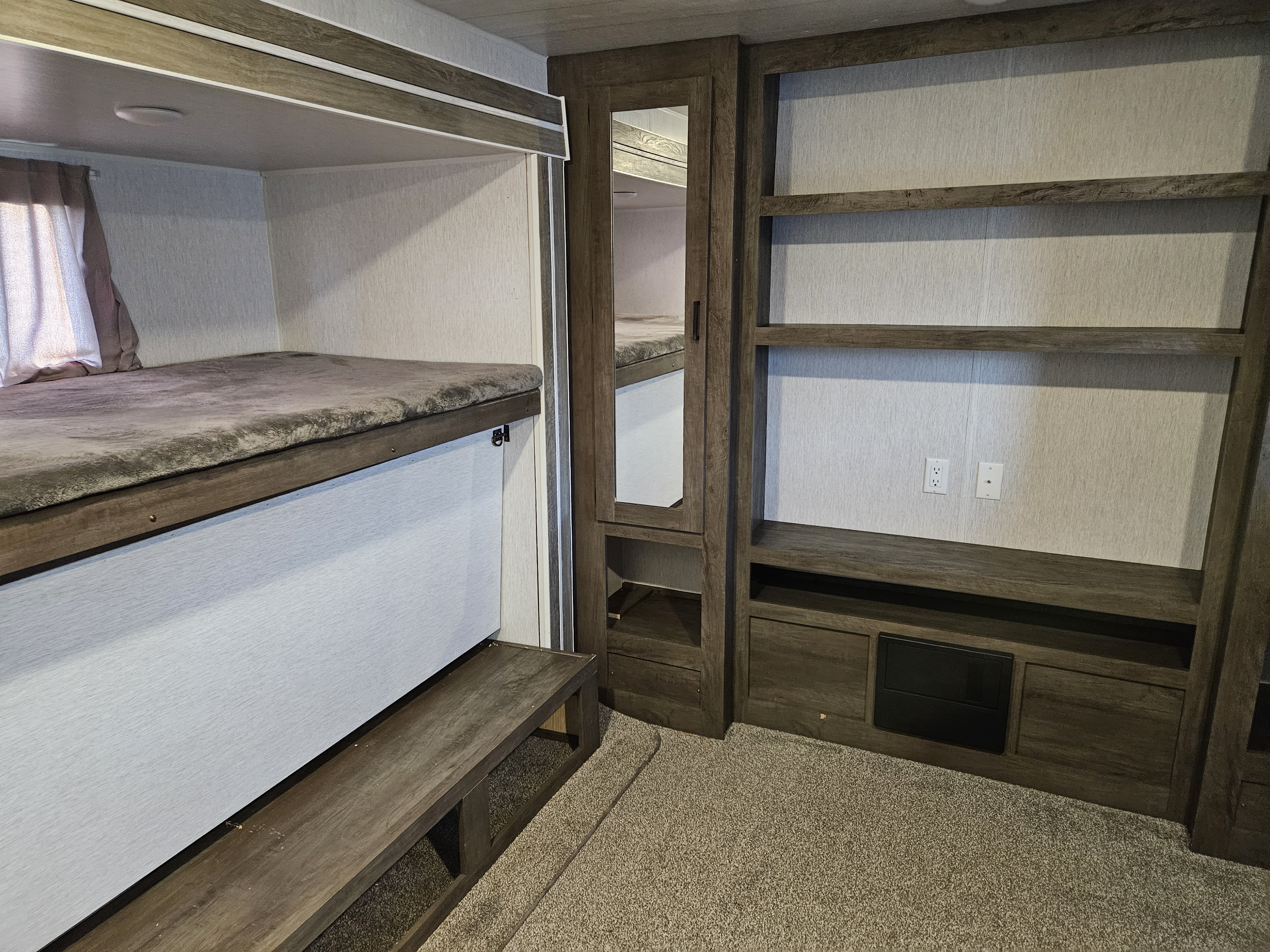 Inside an RV rental: a modern bunkhouse with two comfortable beds, built-in storage shelves, and a mirrored wardrobe.. Forest River Wildwood 2022