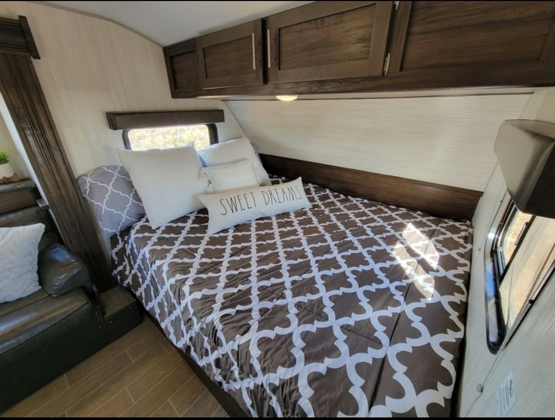 Cozy RV rental bedroom with a neatly made bed, "SWEET DREAMS" pillow, overhead cabinets, and window.. Forest River Wolf Pup 2020