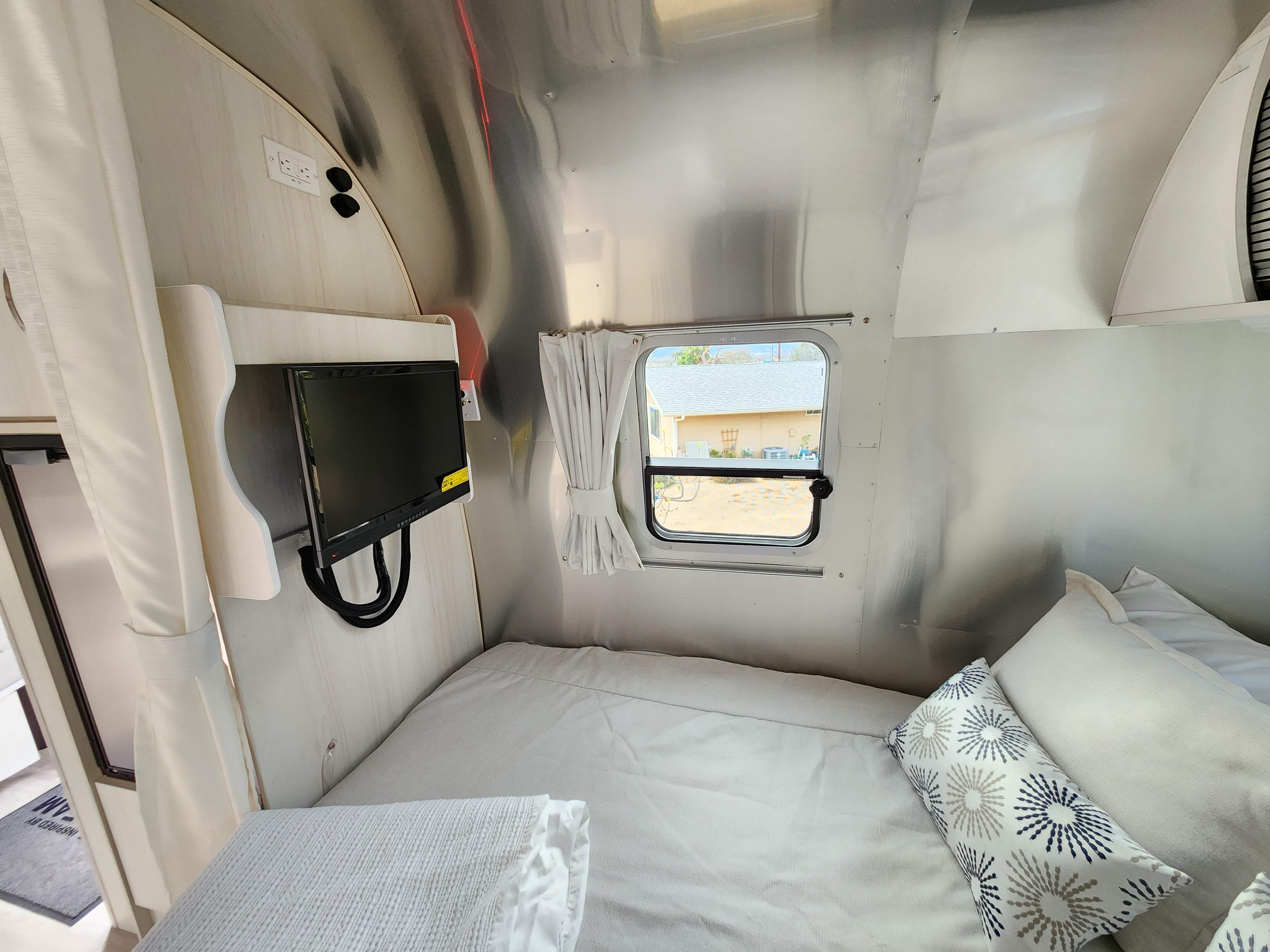 Compact RV rental bedroom featuring a comfy bed, mounted TV, and window view. Ideal for mobile living.. Airstream Bambi 2023