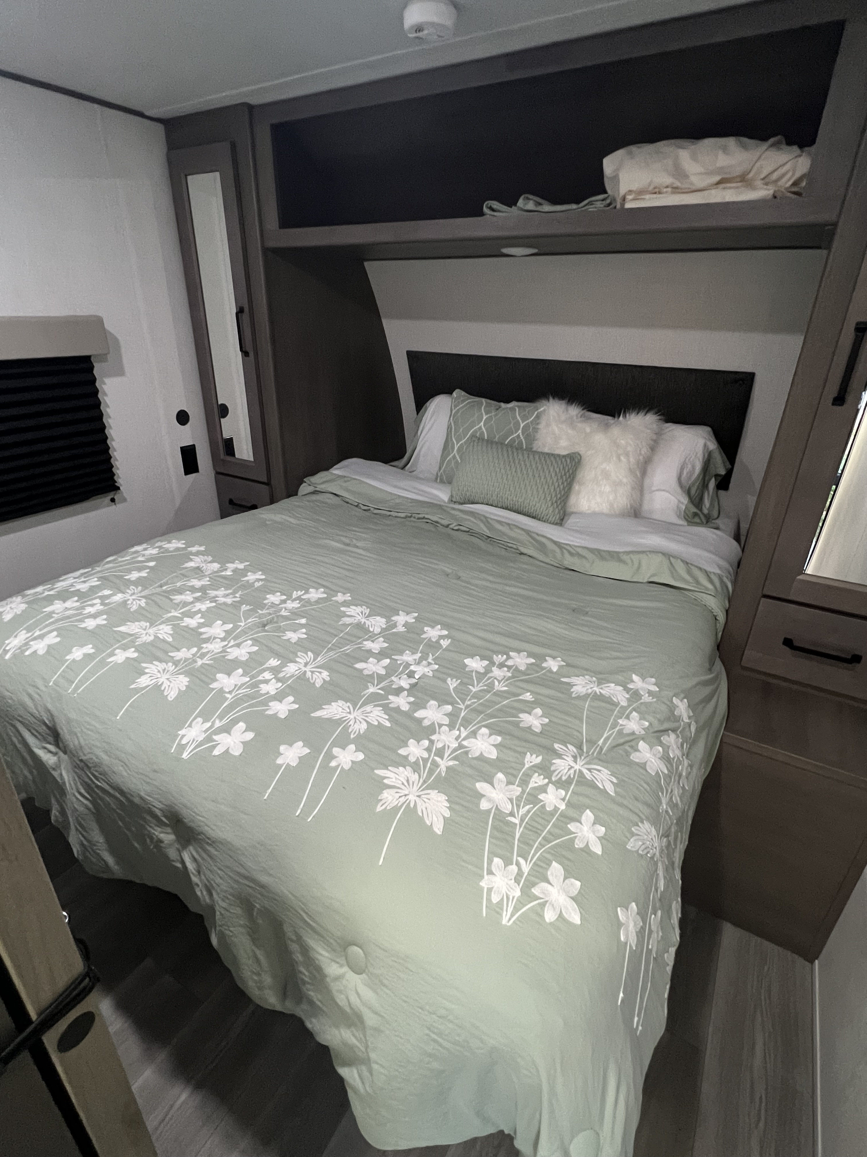 Cozy RV rental bedroom featuring a bed with light green floral bedding, overhead cabinets, and built-in storage.. Grand Design Transcend Xplor 247BH 2024