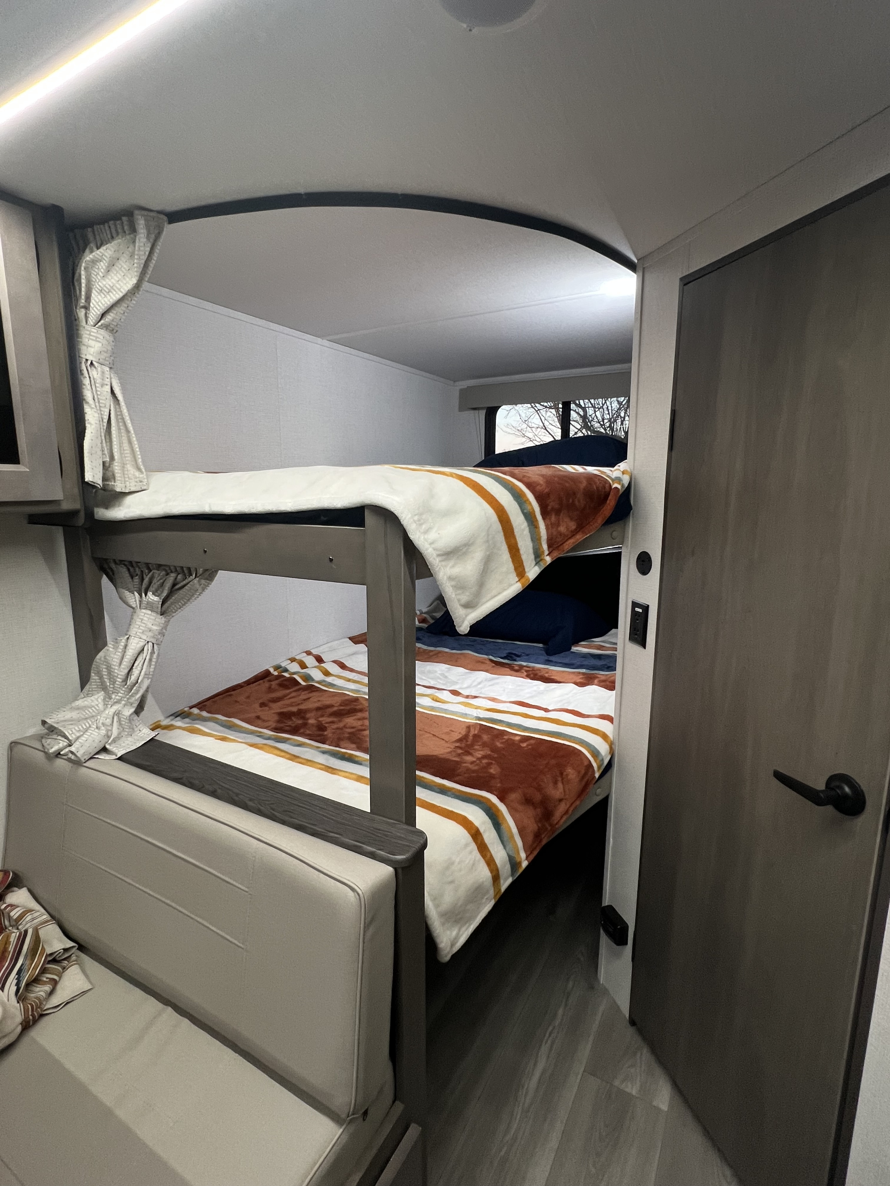 This RV rental features cozy bunk beds with striped blankets, offering comfortable sleeping for your camping or travel adventures.. Grand Design Transcend Xplor 247BH 2024