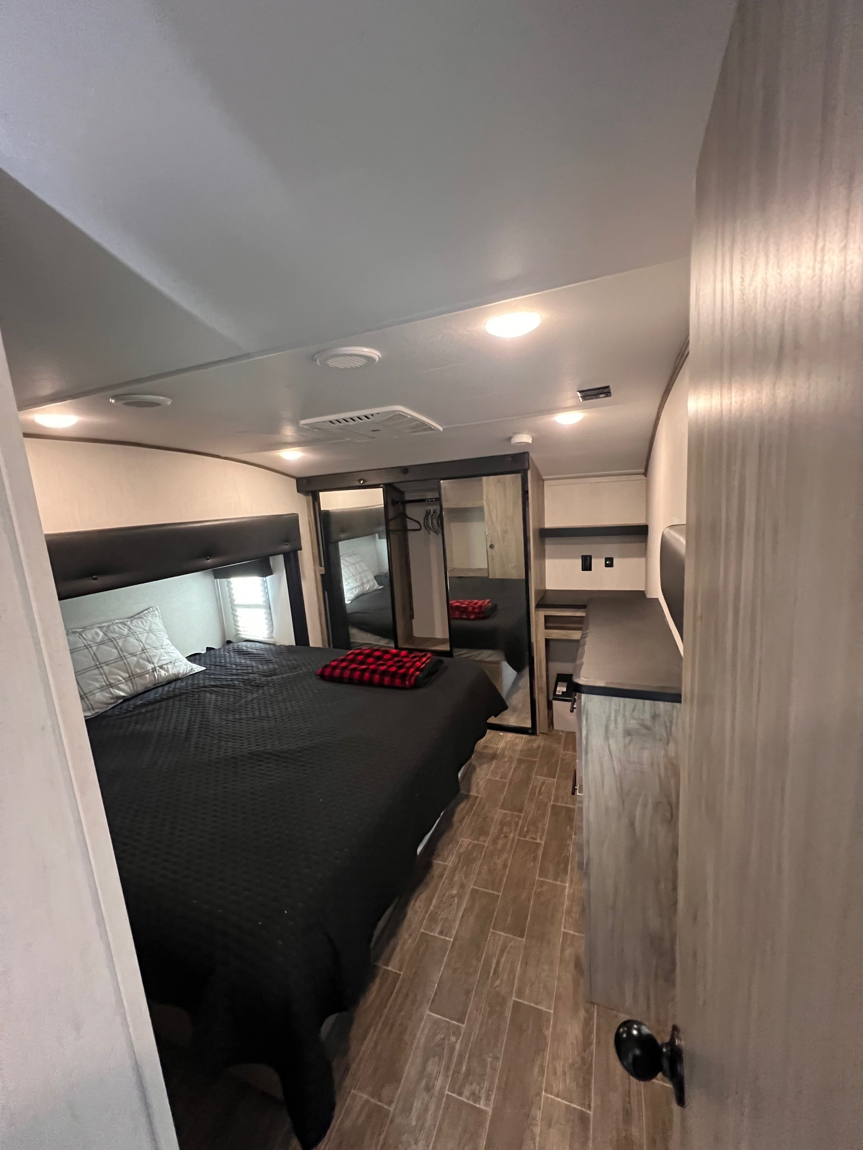 Explore this RV rental bedroom, featuring a black-covered bed, mirror closets, and modern wood-style flooring.. Forest River Cherokee Arctic Wolf 2022