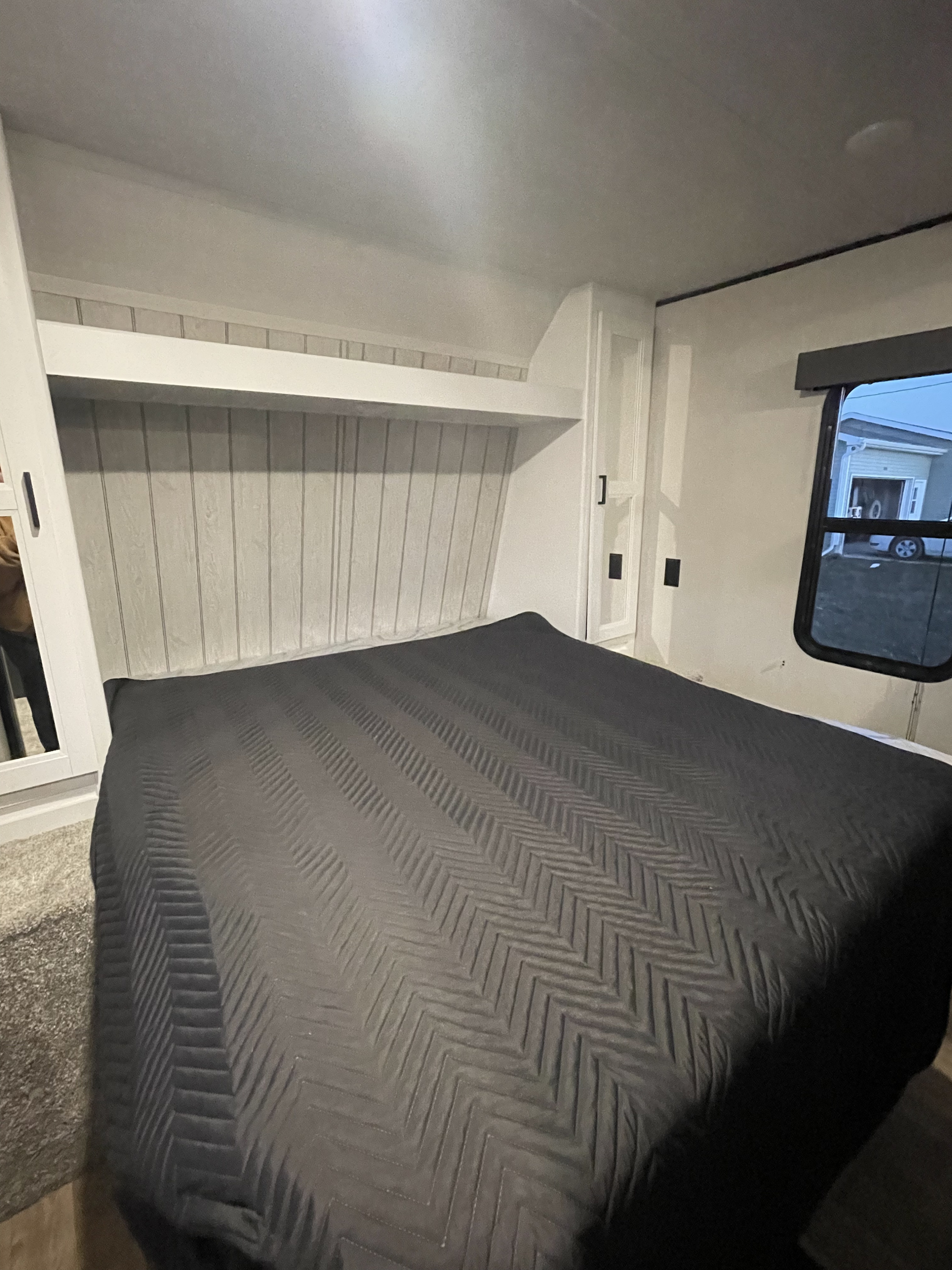Inside this RV rental: a compact bedroom featuring a dark, chevron-quilted bed, built-in storage, and window.. Keystone RV Hideout 2022