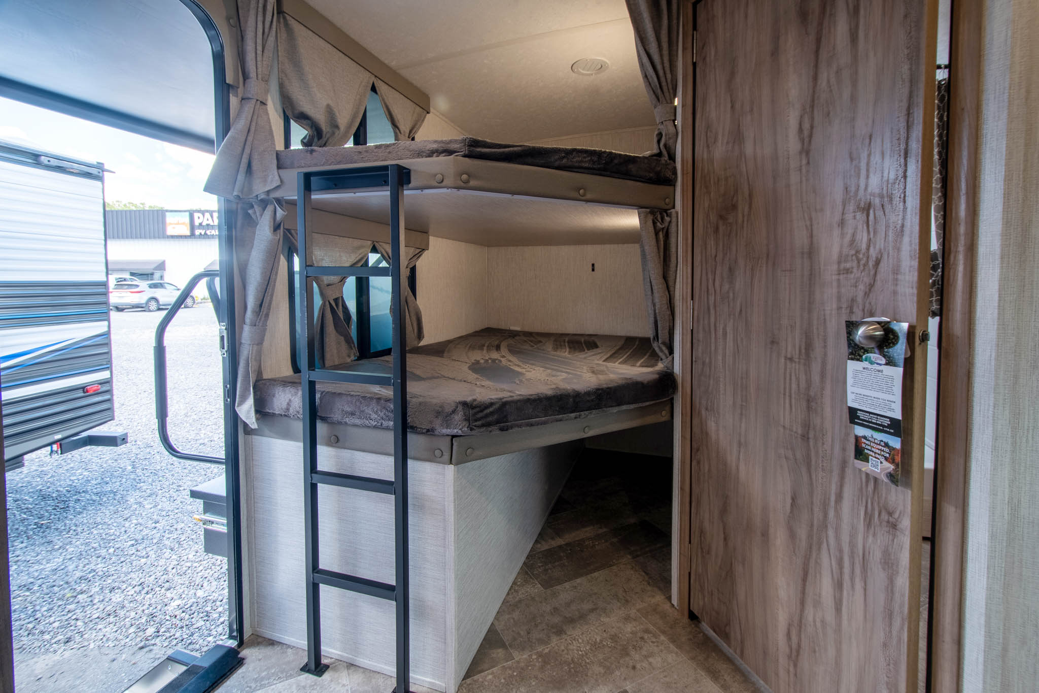 Inside an RV rental: cozy bunk beds, ladder, and view out the entry. Ideal for family road trips in this travel trailer.. Palomino Solaire Ultra Lite 2023