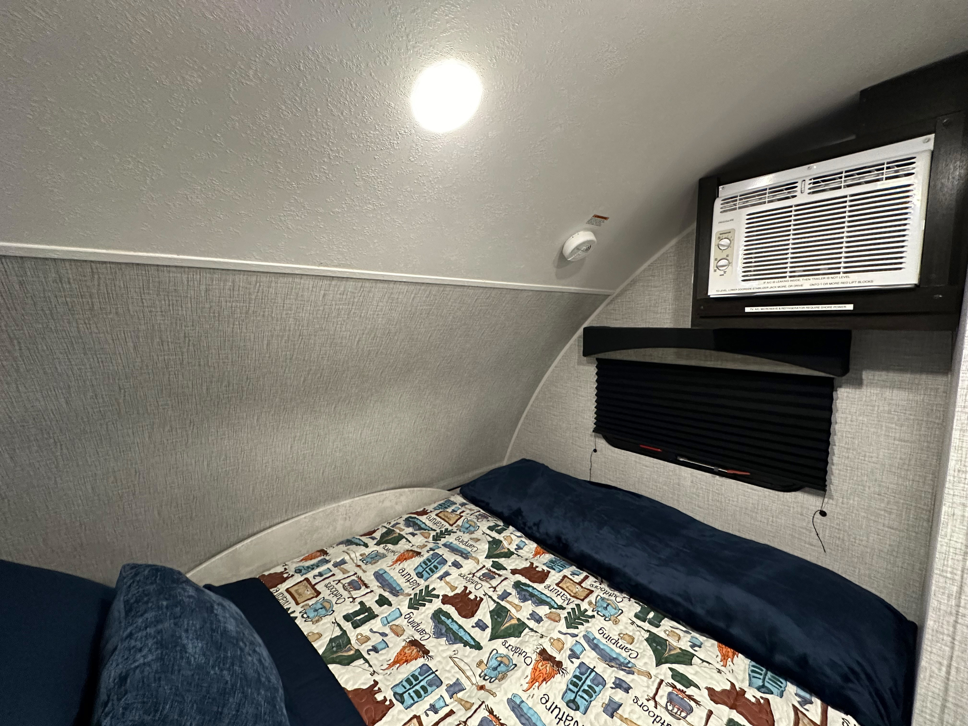 Cozy RV rental bedroom featuring a bed with a camping-themed blanket, wall-mounted AC unit, and smoke detector.. Braxton Creek Bushwhacker Plus 15DS 2022