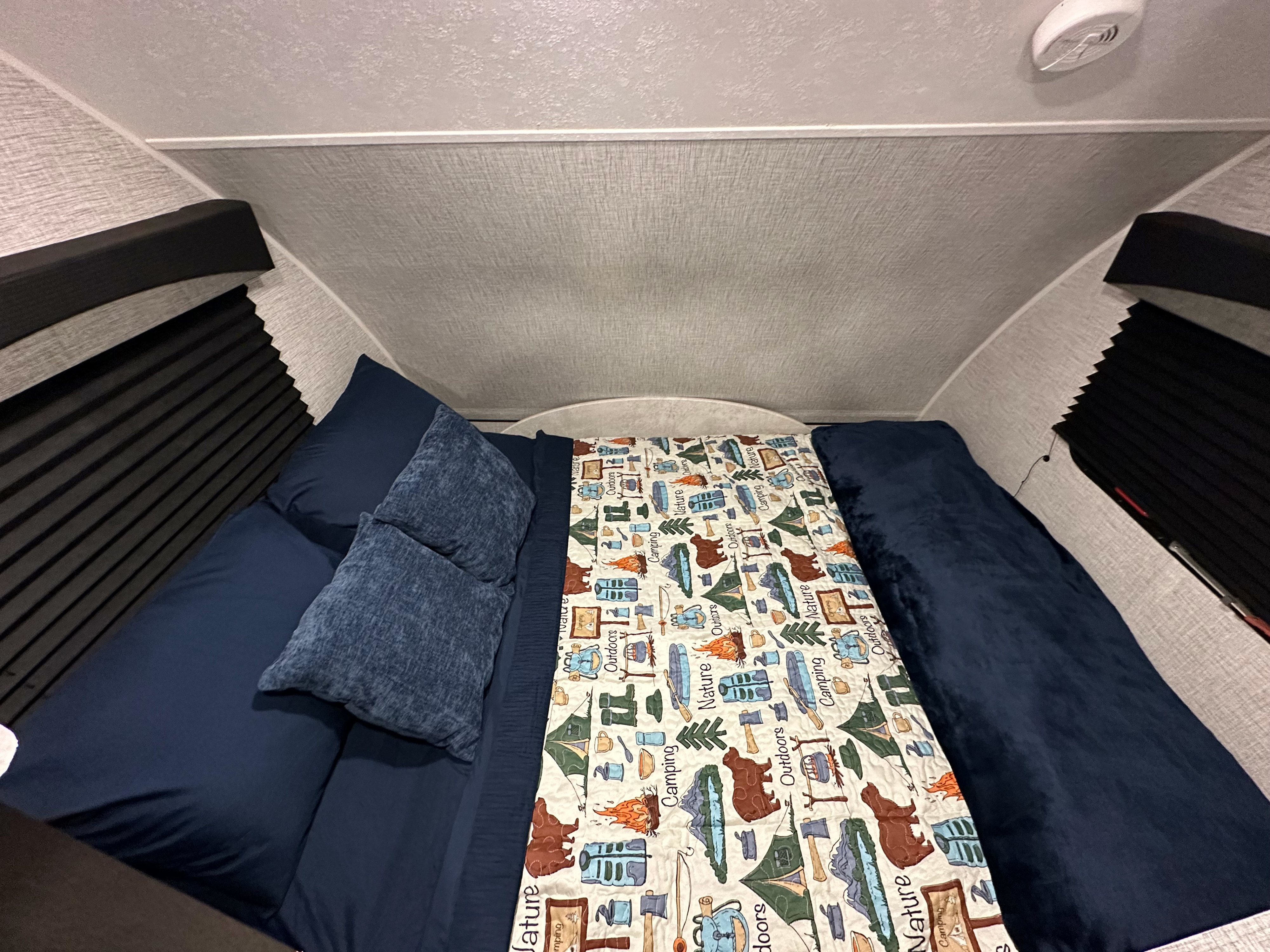 Cozy RV rental bedroom with dark blue bedding and a nature-themed quilt, featuring compact design and window blinds.. Braxton Creek Bushwhacker Plus 15DS 2022
