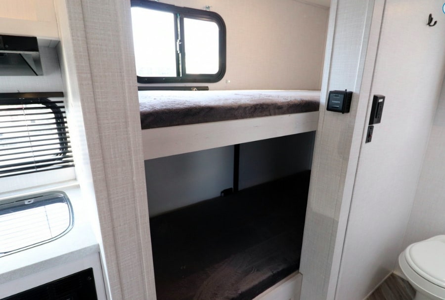 RV rental's cozy interior: bunk beds for sleeping, a compact kitchen, and a nearby bathroom.. Dutchmen Coleman Rubicon 2022